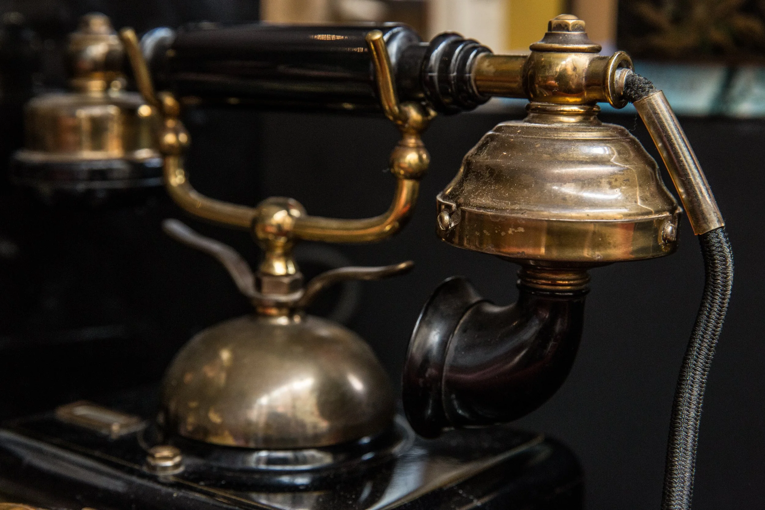 Close-up of an antique brass telephone with a black handle and a cord, showing detailed metallic parts against a dark background.