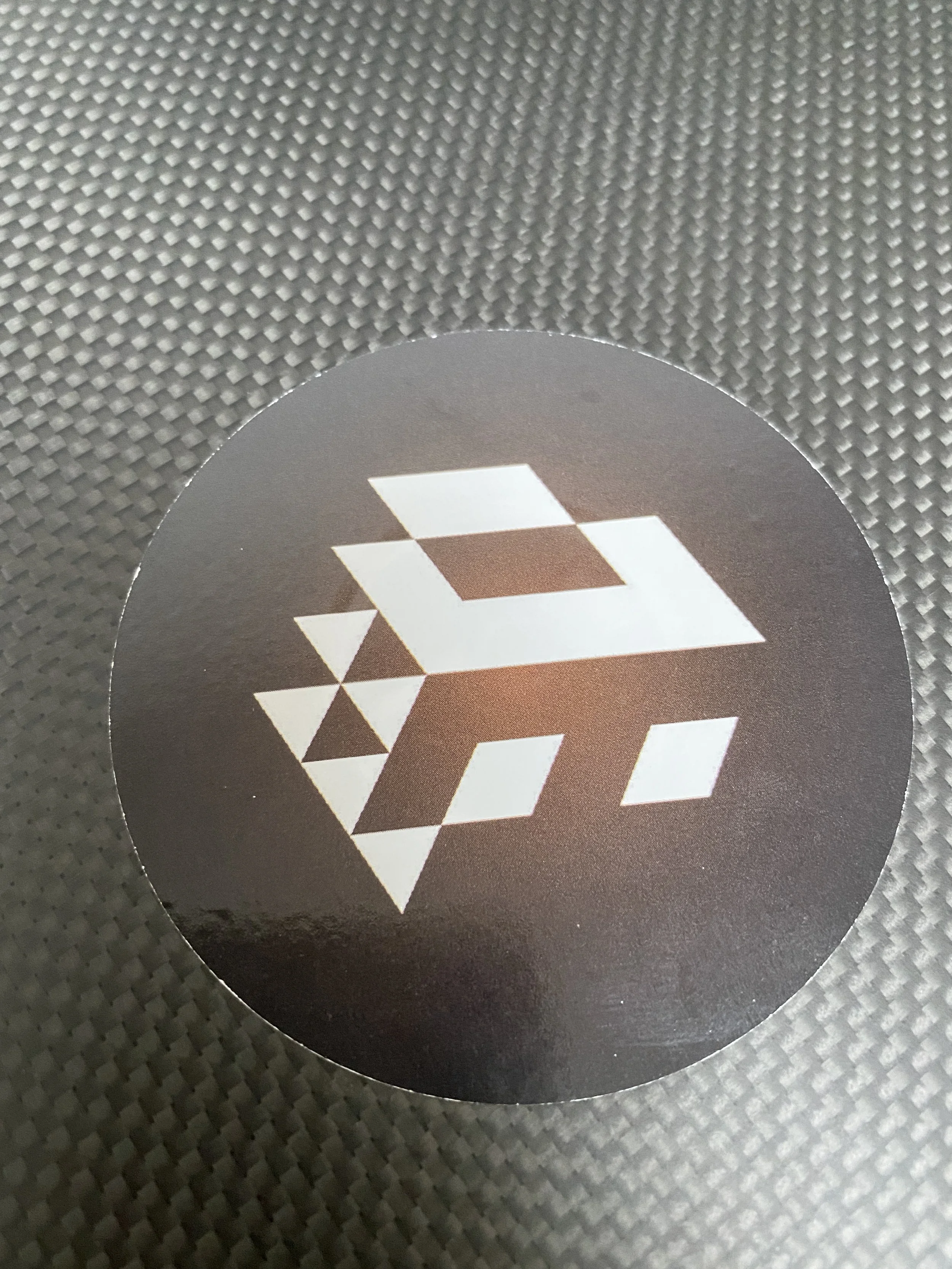 Close-up of a black circular sticker with white geometric design, placed on a textured surface.