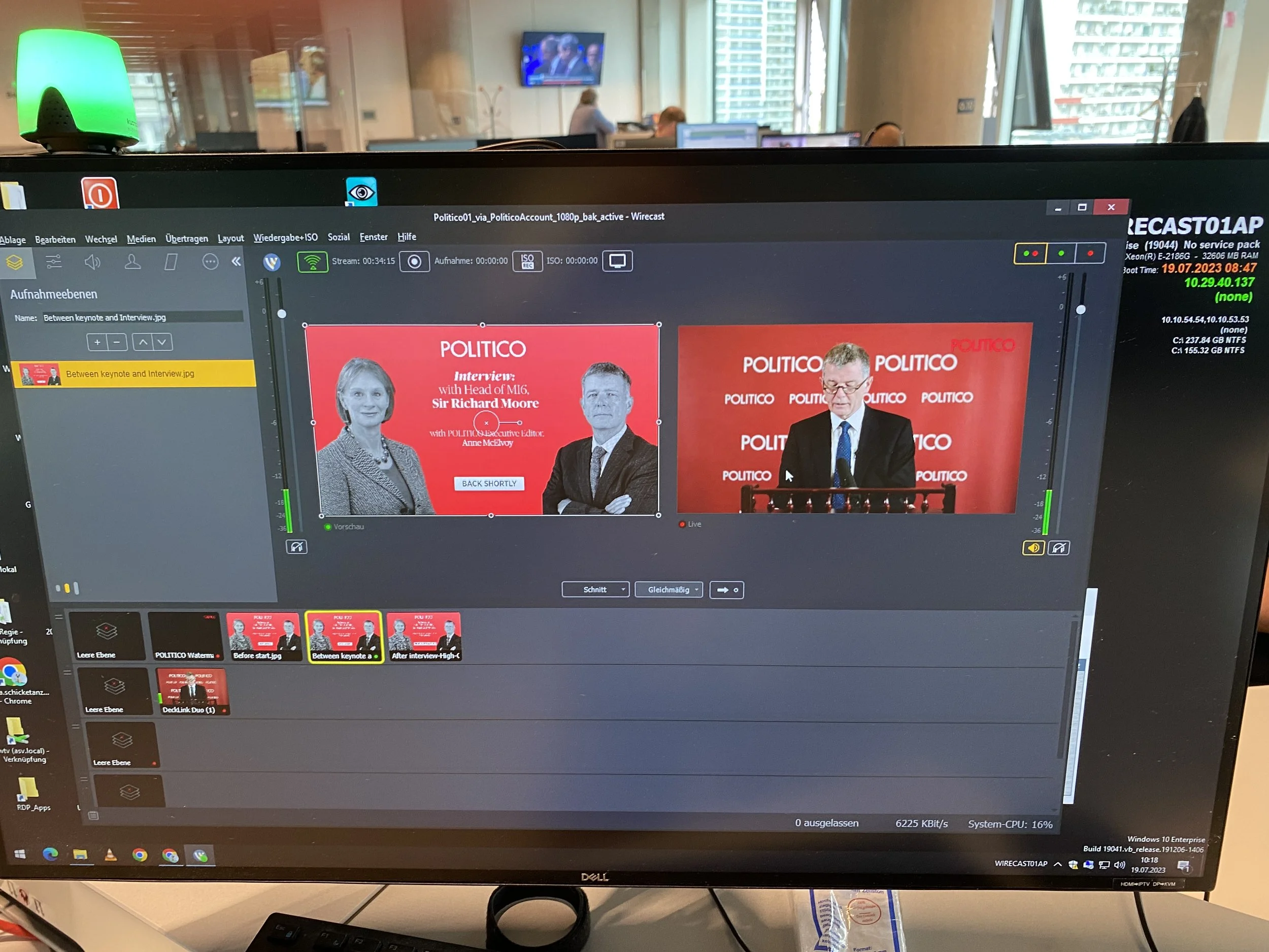 Computer screen showing a video conference setup with an active interview presentation on Politico, featuring images of two individuals against a red background, with various software controls and files visible on the desktop.