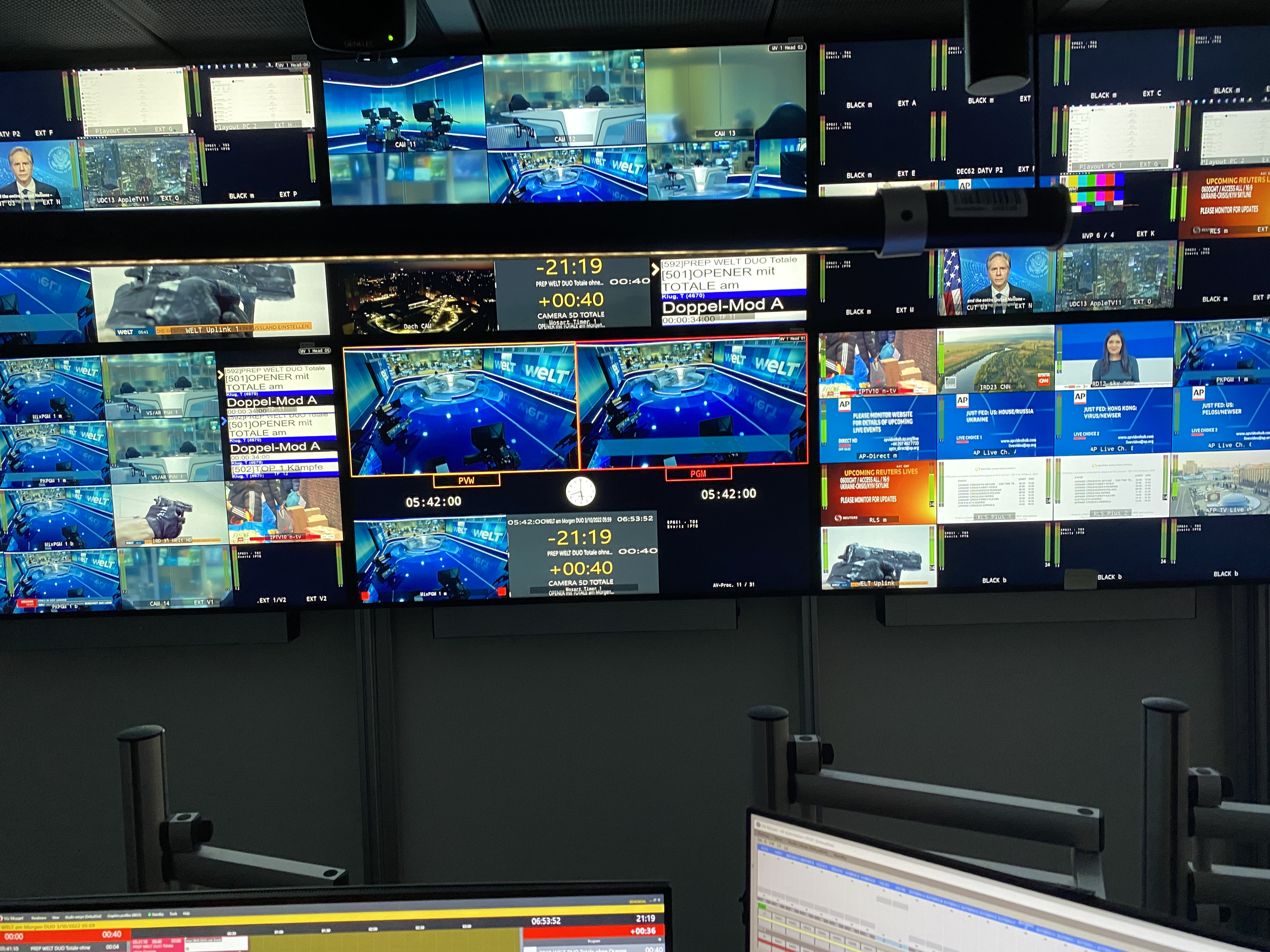 Multiple television screens displaying news, weather, and live camera feeds in a control room setting.