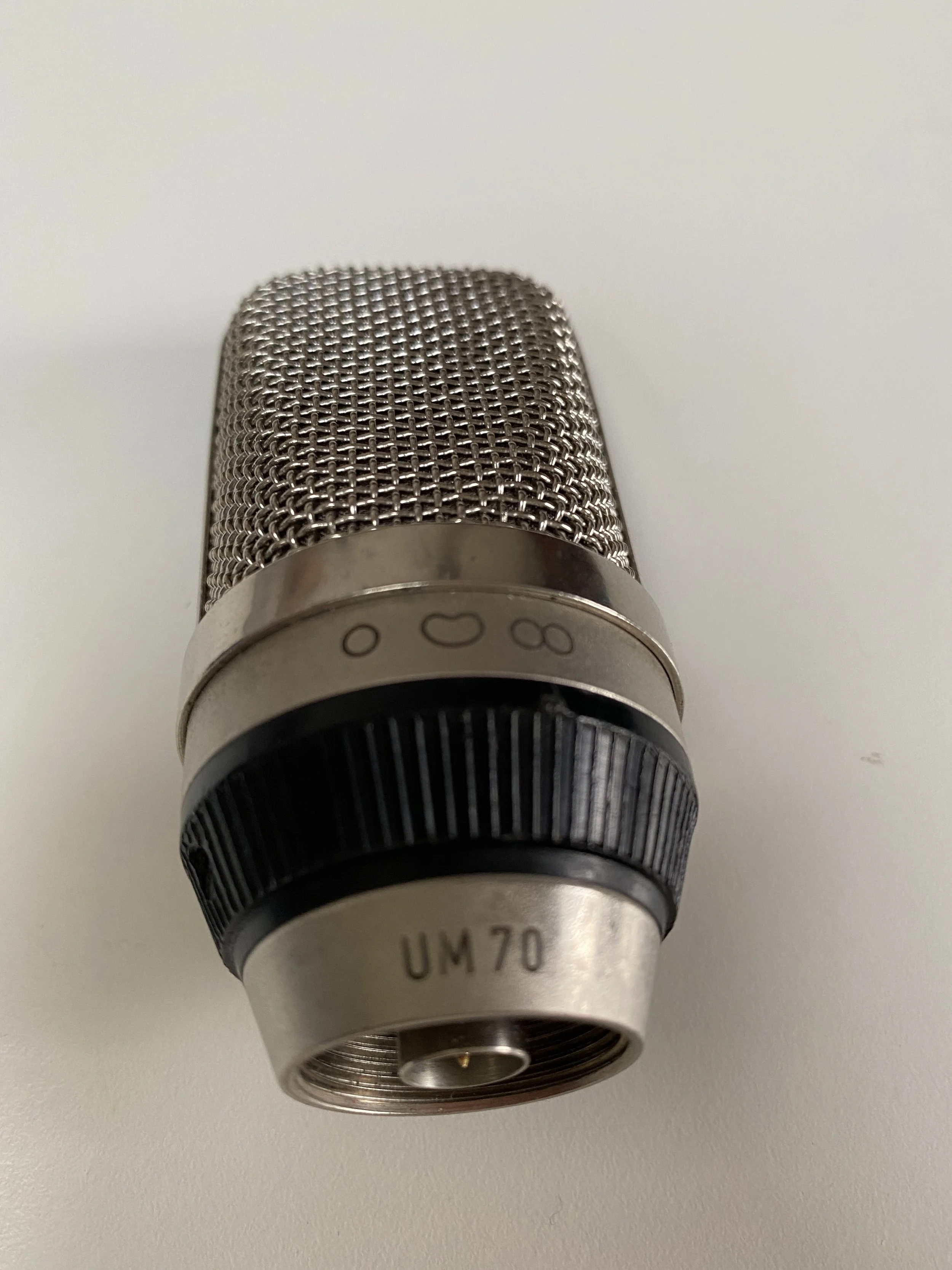 Close-up of a metal microphone with a black and silver design, viewed upside down on a plain white surface.