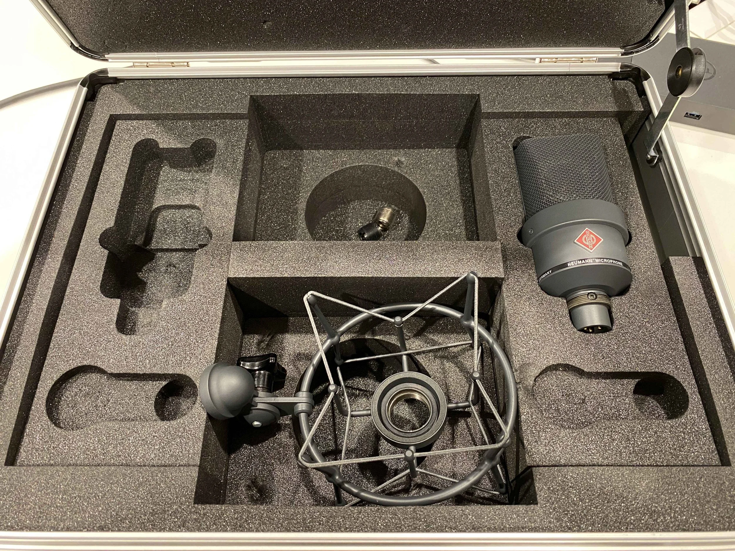 Open black foam-lined case containing a microphone, cables, and foam cutouts for securing equipment.