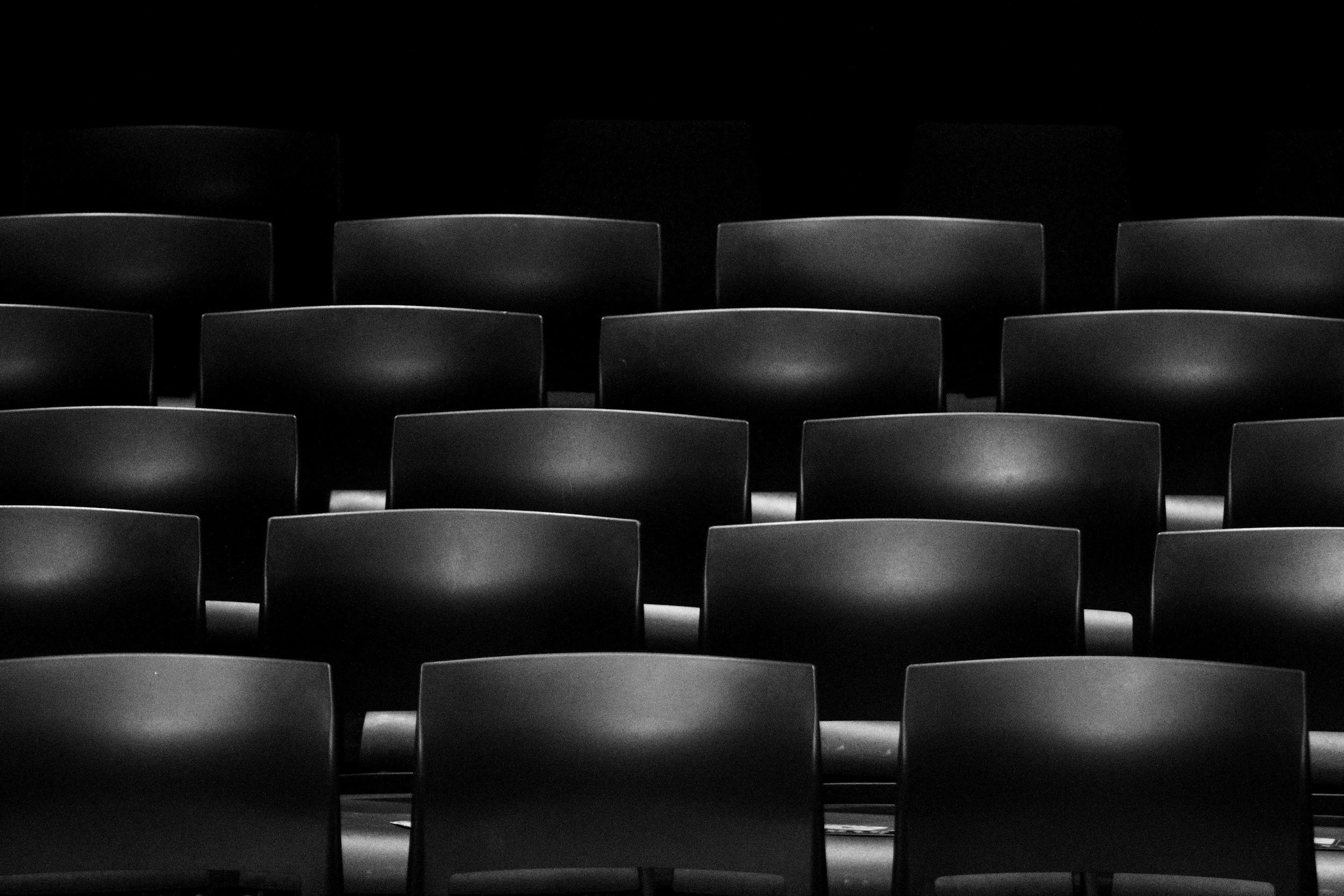 Multiple black chairs arranged in rows in a dimly lit room.