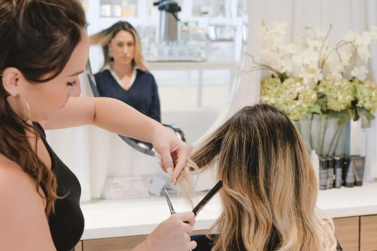 Friseur schneidet die Haare einer Kundin in einem Salon, im Hintergrund stehen Blumen und ein Spiegel.