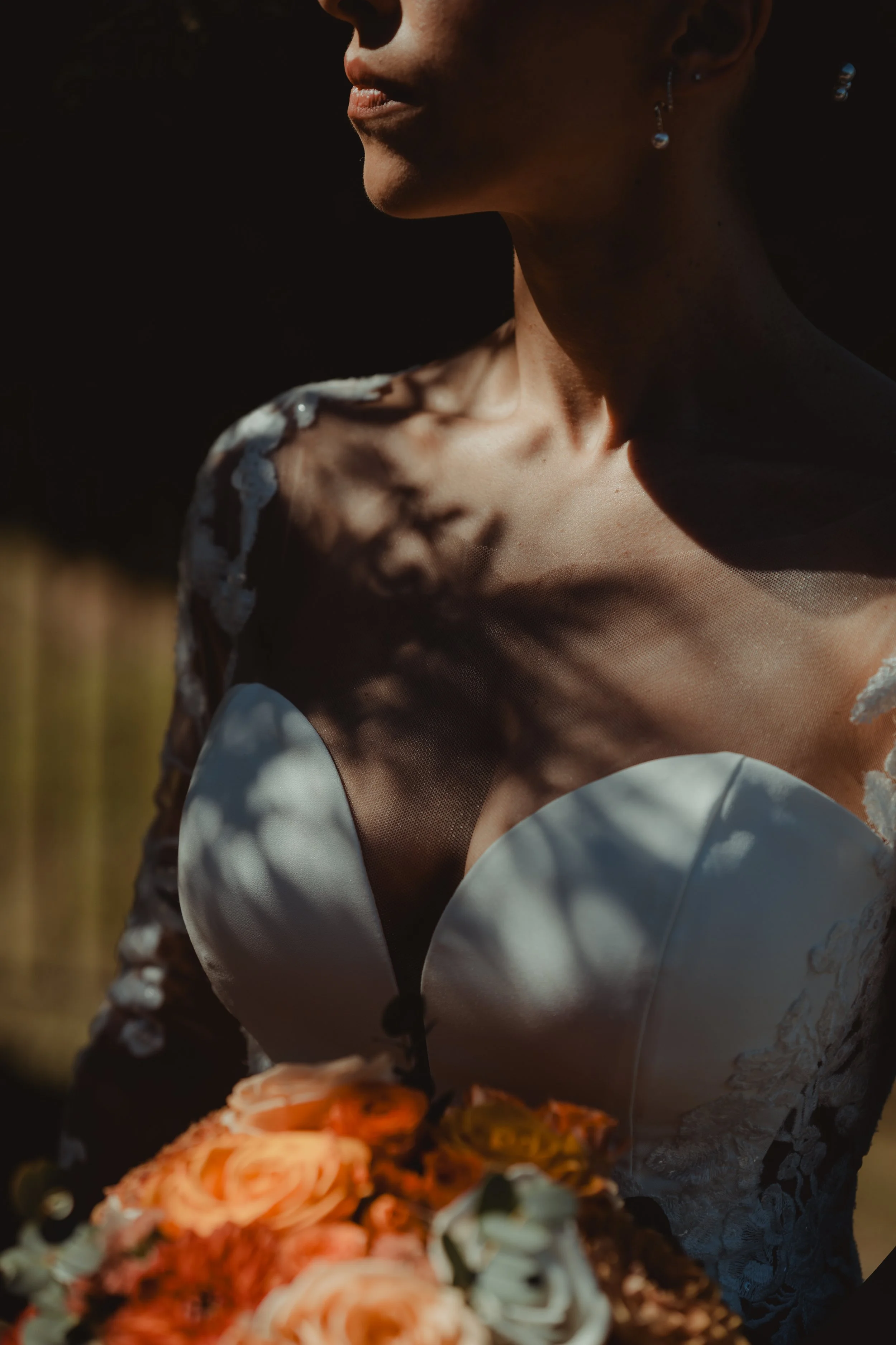 Dettaglio di una donna con orecchini di perline e un vestito con dettagli di pizzo, che si trova all'aperto con sfondo sfocato.