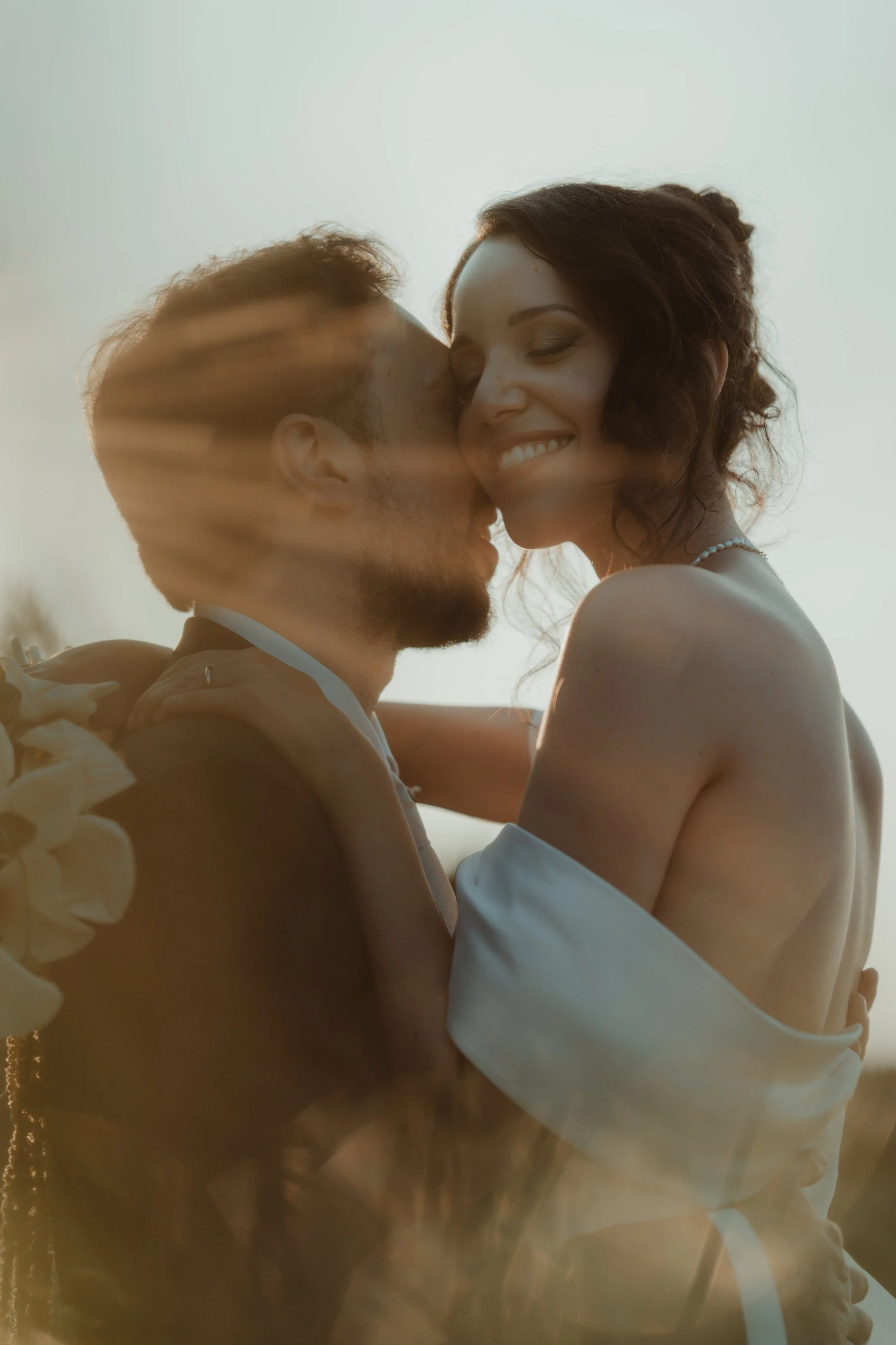 Una coppia innamorata si abbraccia e sorride con gli occhi chiusi, con il sole che tramonta sullo sfondo.