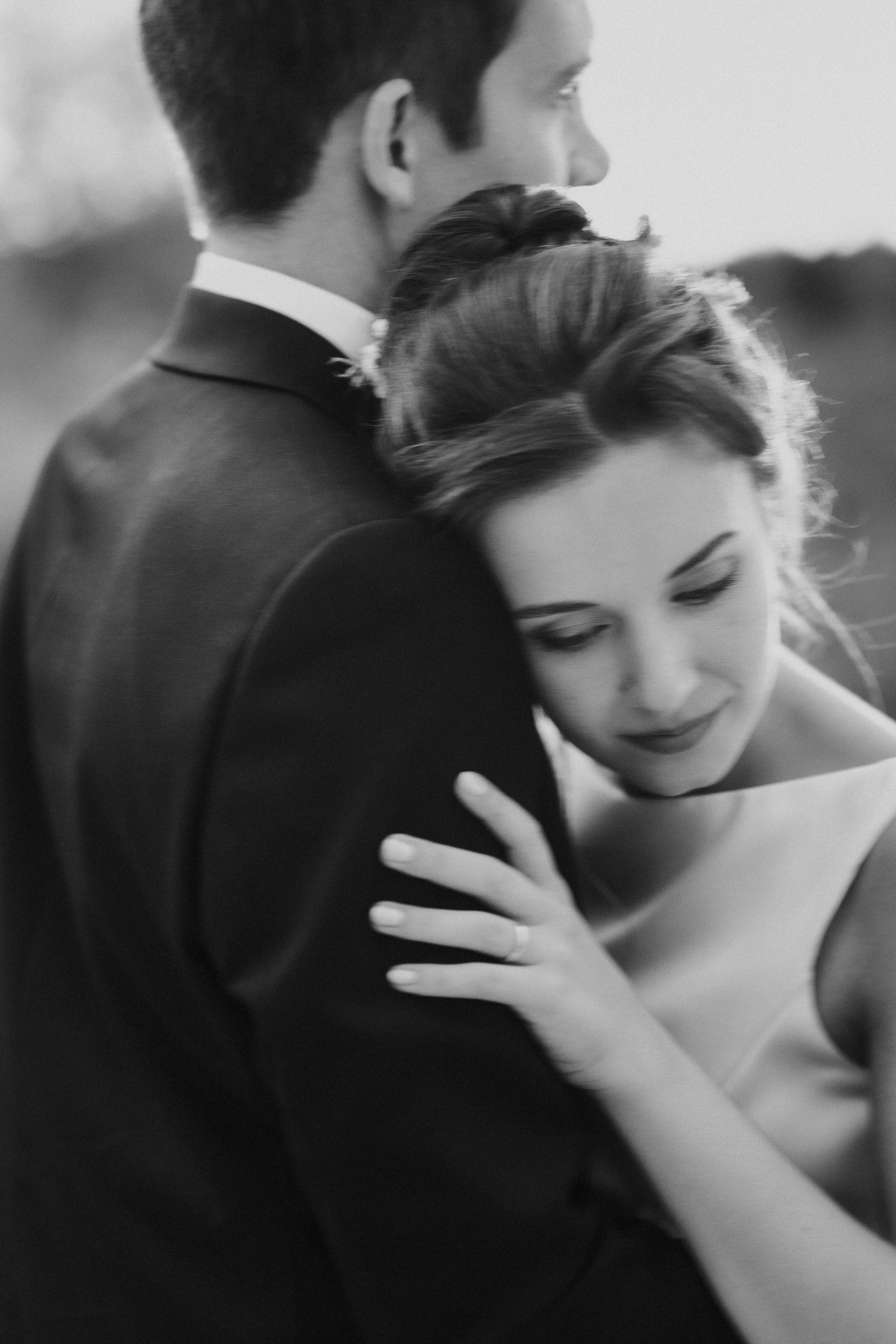 Una coppia si abbraccia, lei sorride dolcemente mentre lui si rivolge leggermente di lato, in un'immagine in bianco e nero.