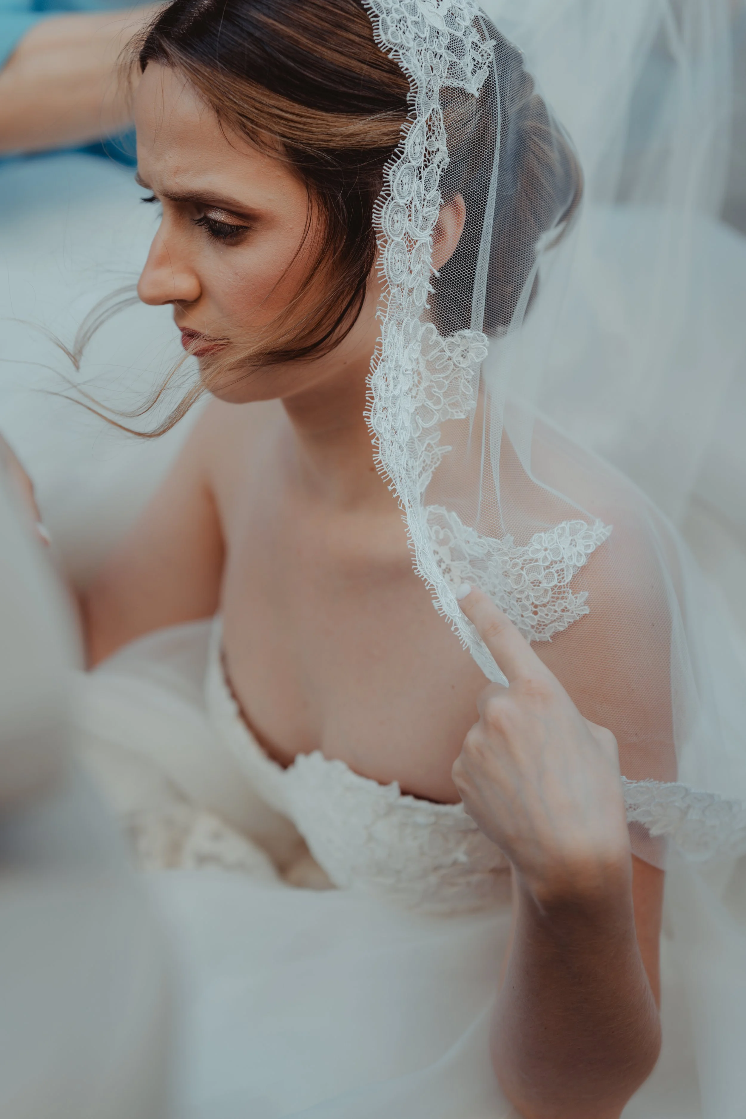 Primo piano di una donna con il trucco naturale, con un velo da sposa bianco con dettagli in pizzo, che si prepara probabilmente per il matrimonio.