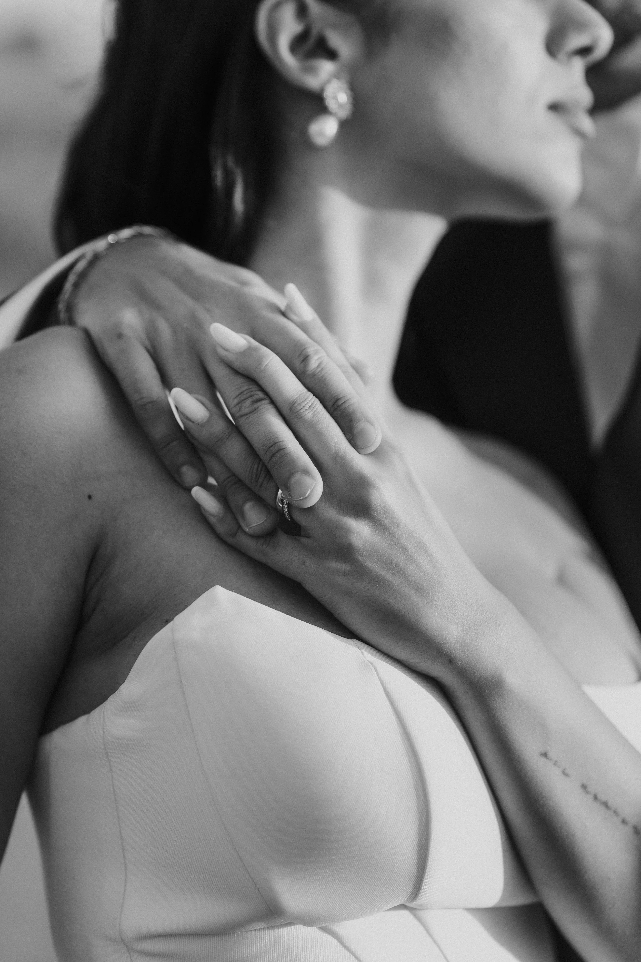 Dettaglio di una donna in abito bianco con orecchini pendenti, che si tiene la spalla