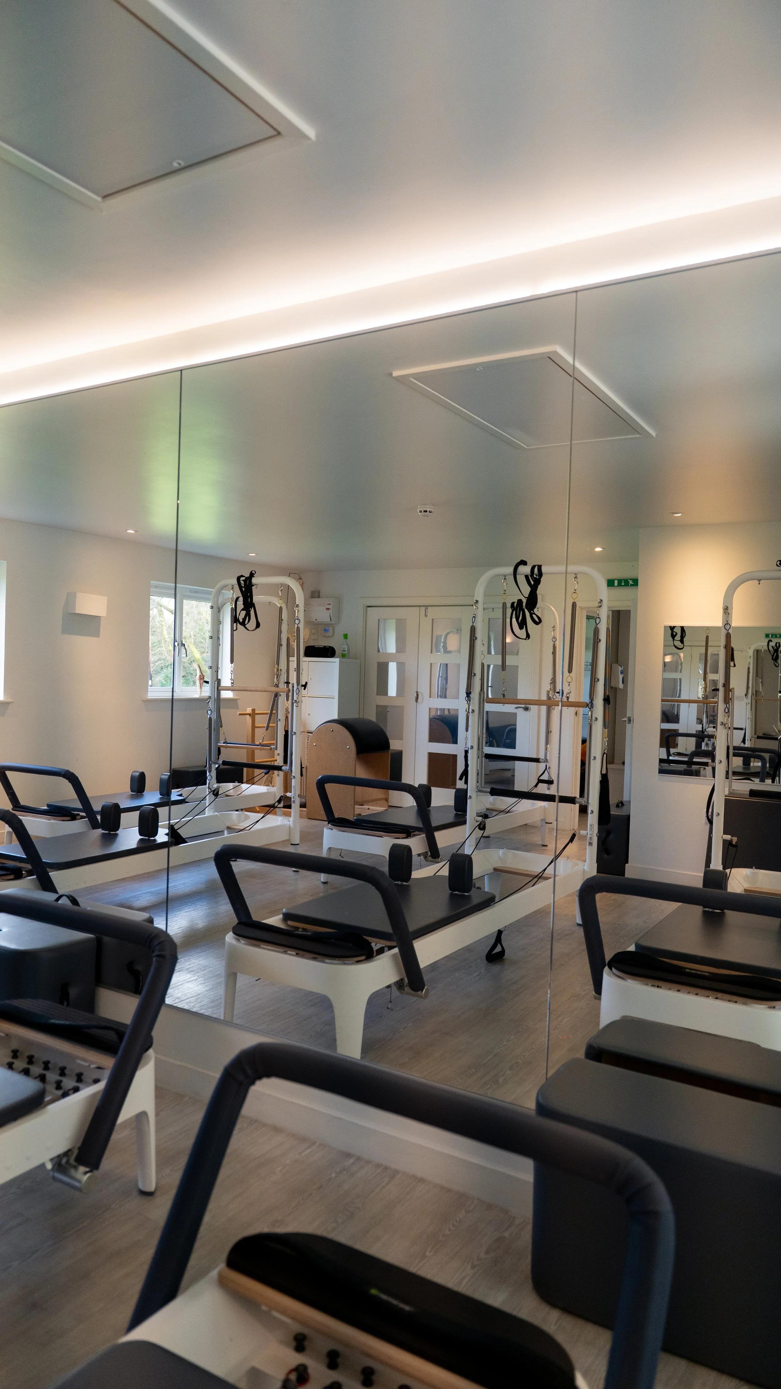 Fitness studio with Pilates reformer machines, mirrors, and window with natural light.