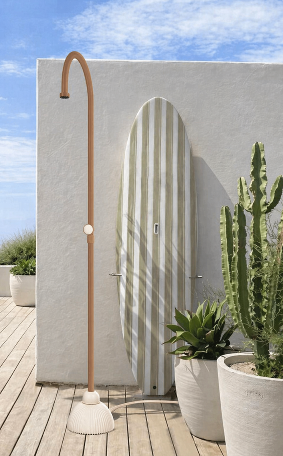 An outdoor patio scene featuring a surfboard leaning against a white wall, a tall, curved outdoor shower with a copper-colored pipe, and two white planters with green succulents and cacti, under a partly cloudy sky.