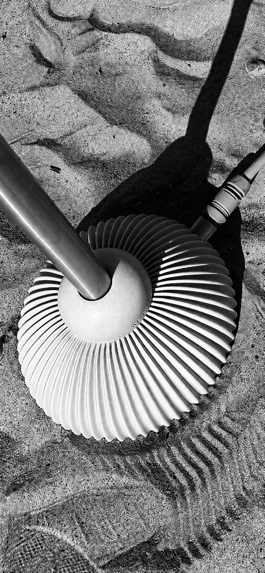 Close-up of a vintage metal fan lying on sandy ground, with a person's foot nearby and a shadow cast over the scene.