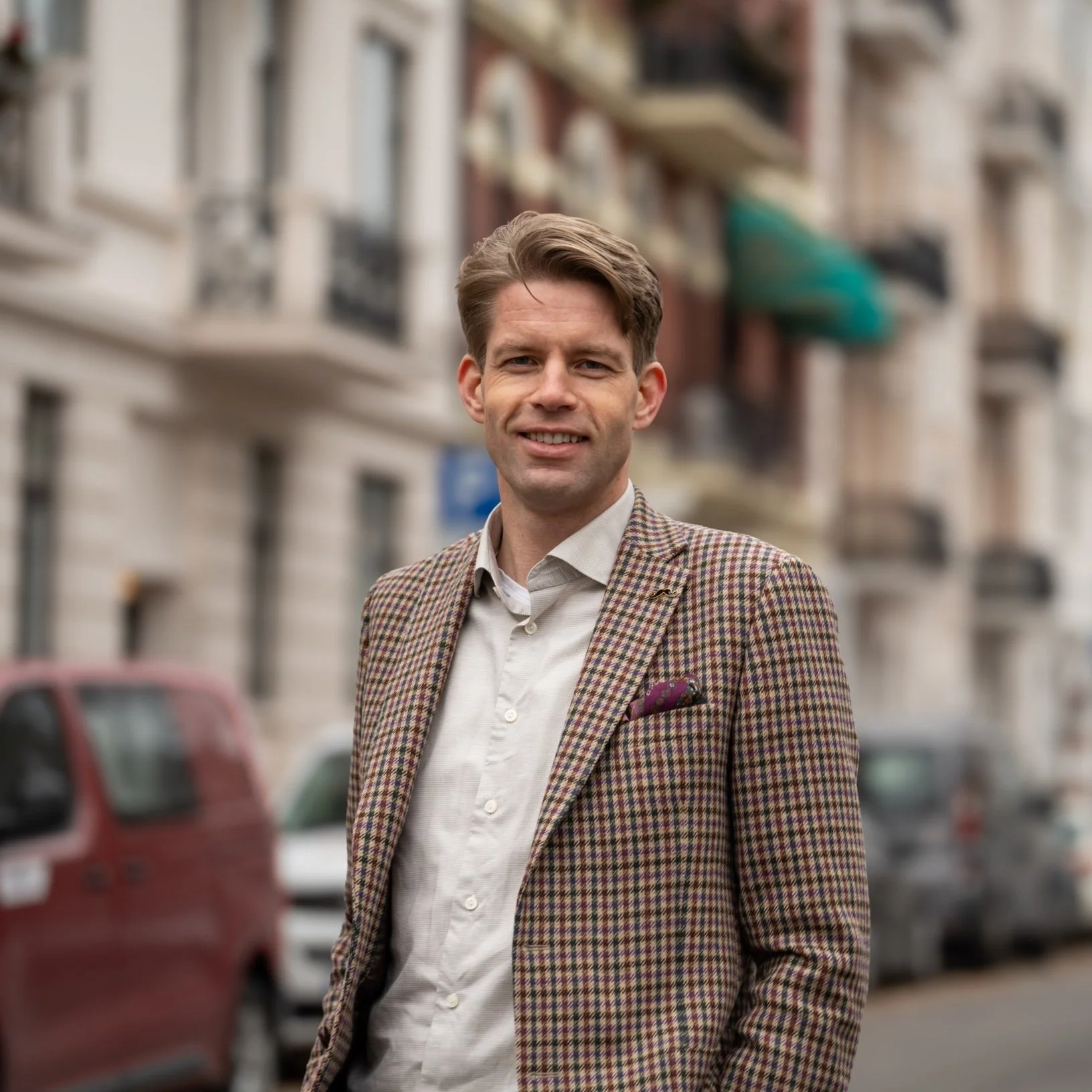 En mann i dress på en gate med biler parkert langs veien.
