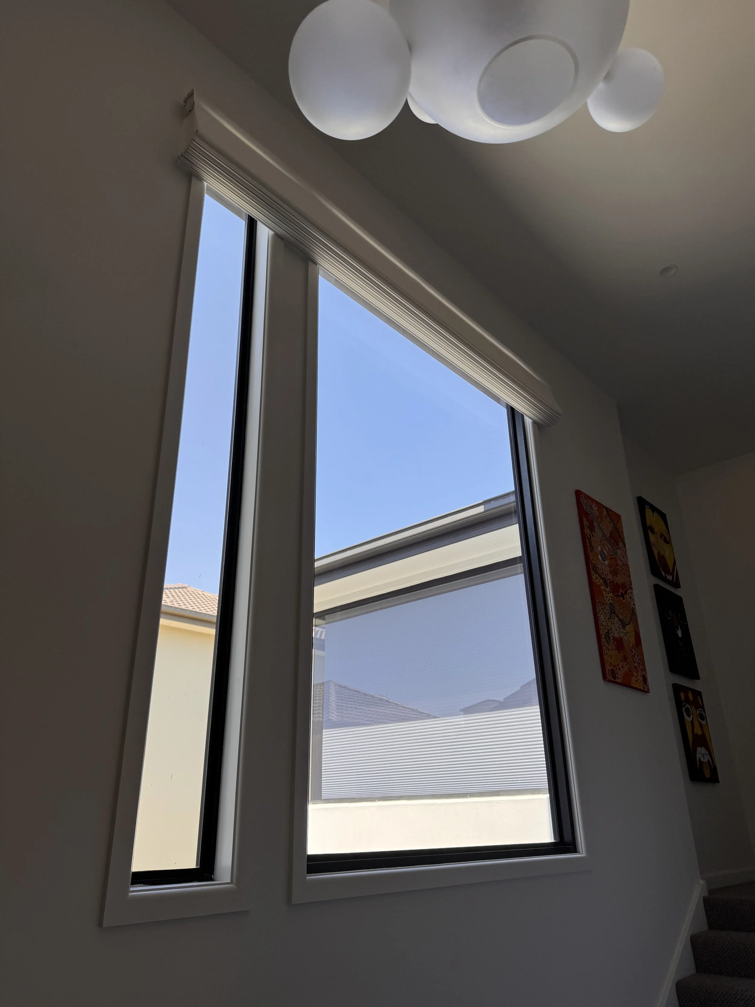 Interior view of a window with white blinds and a view of neighboring houses and blue sky outside.