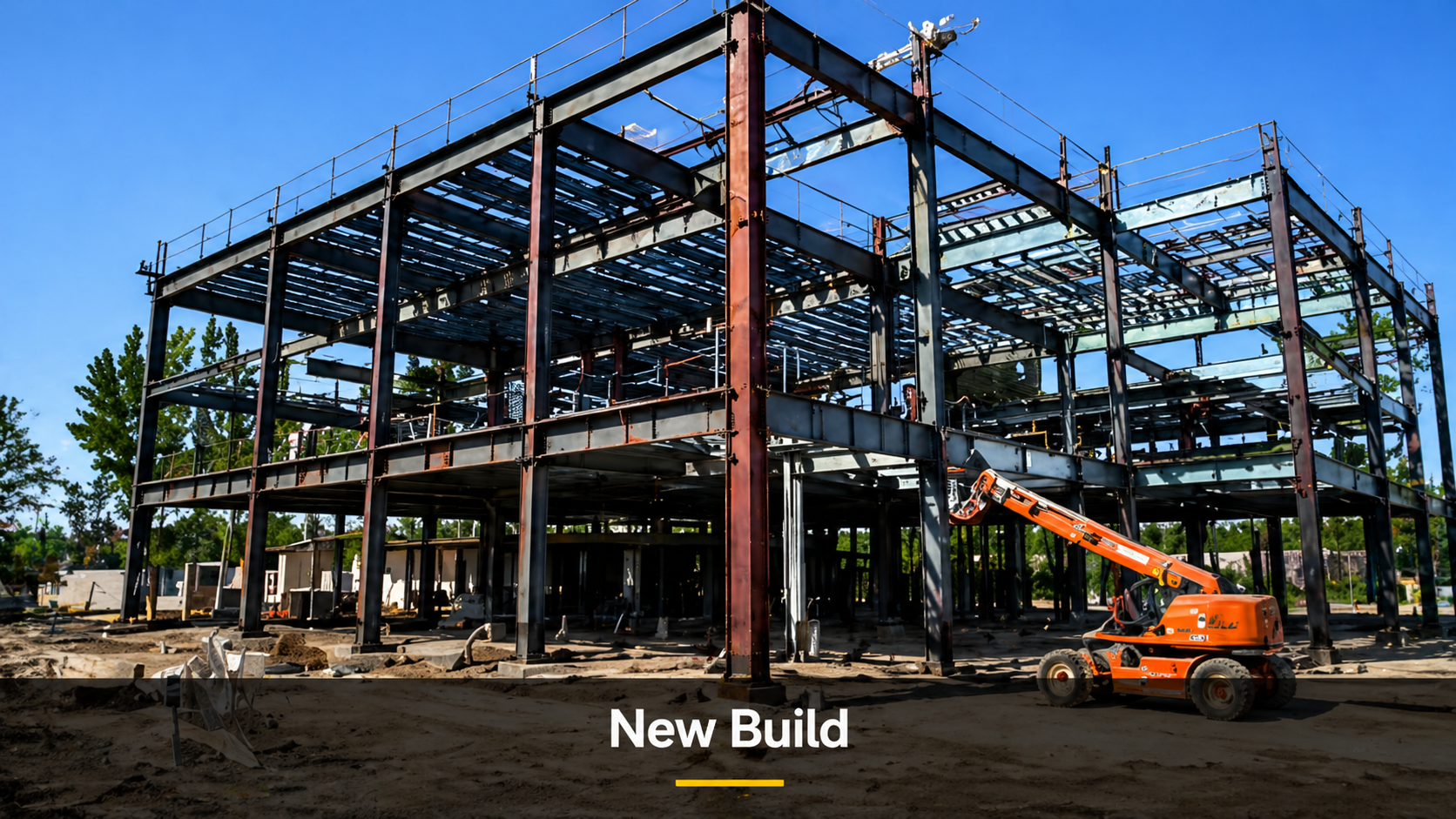 Construction site with a steel frame structure of a new building, a small orange construction lift equipment on the ground, and green trees in the background under a clear blue sky.