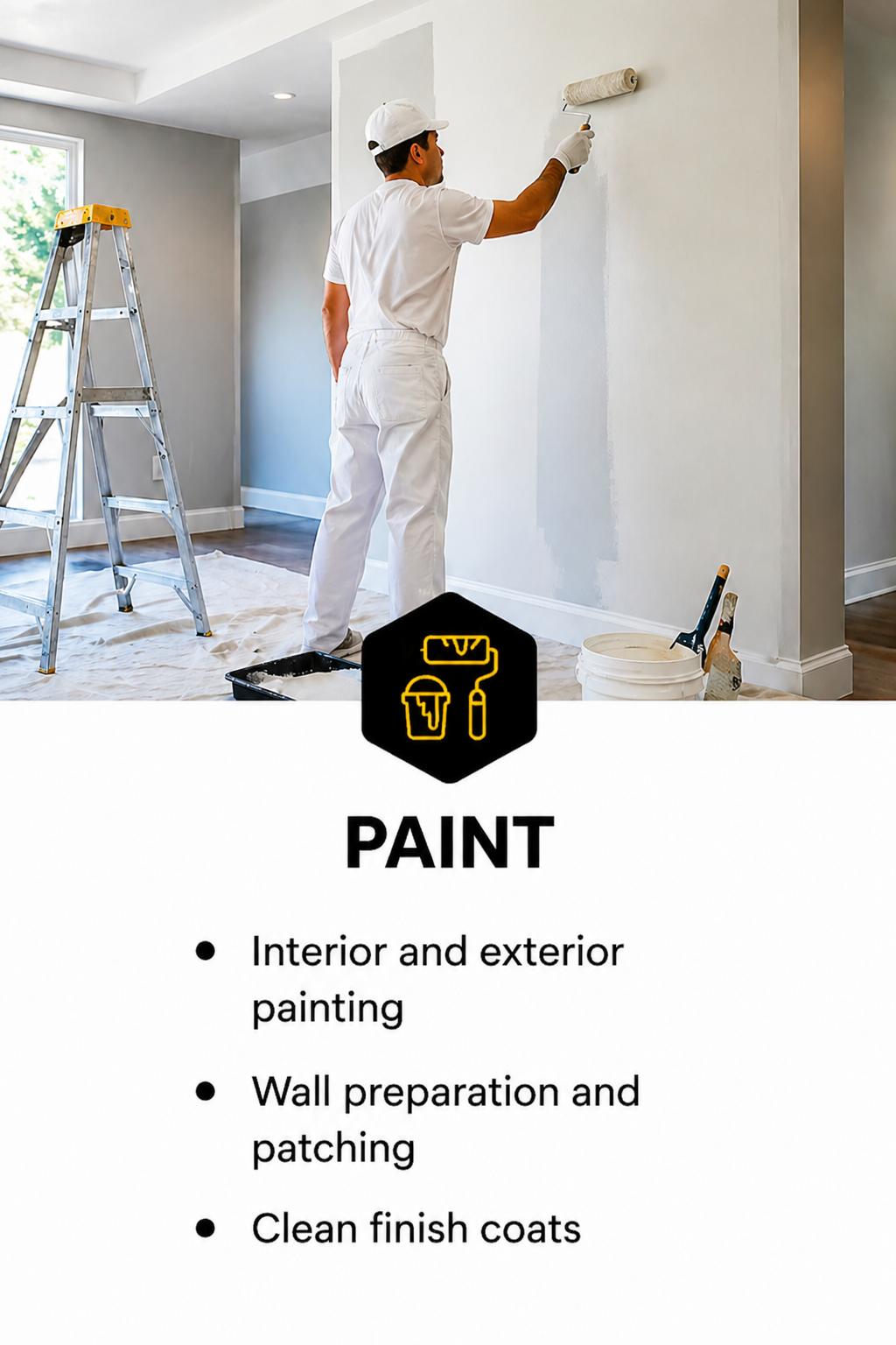 A person painting a wall with a roller brush, standing near a ladder in a room with a large window. There are painting supplies on the floor including a bucket, brushes, and a paint tray.