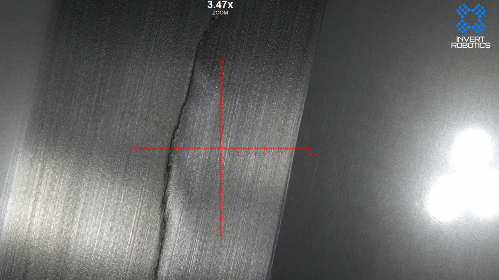 A close-up view of a metallic surface with a crack, measured with a red overlay showing the scale from 0 to 10 millimeters, with the logo of Invert Robotics in the top right corner.