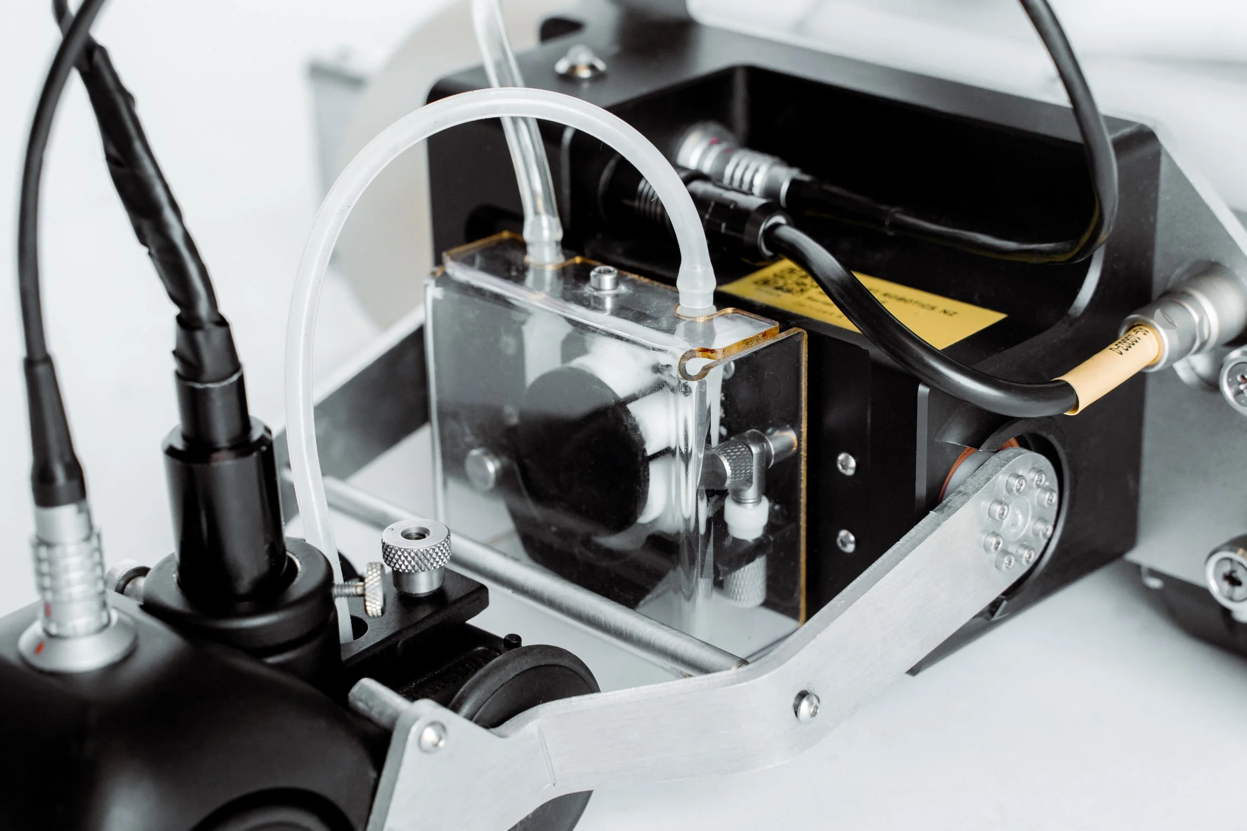 Close-up of a ultrasonic equipment setup featuring metal and plastic parts, tubing, and connectors in a laboratory or technical environment. on an invert robotics robot