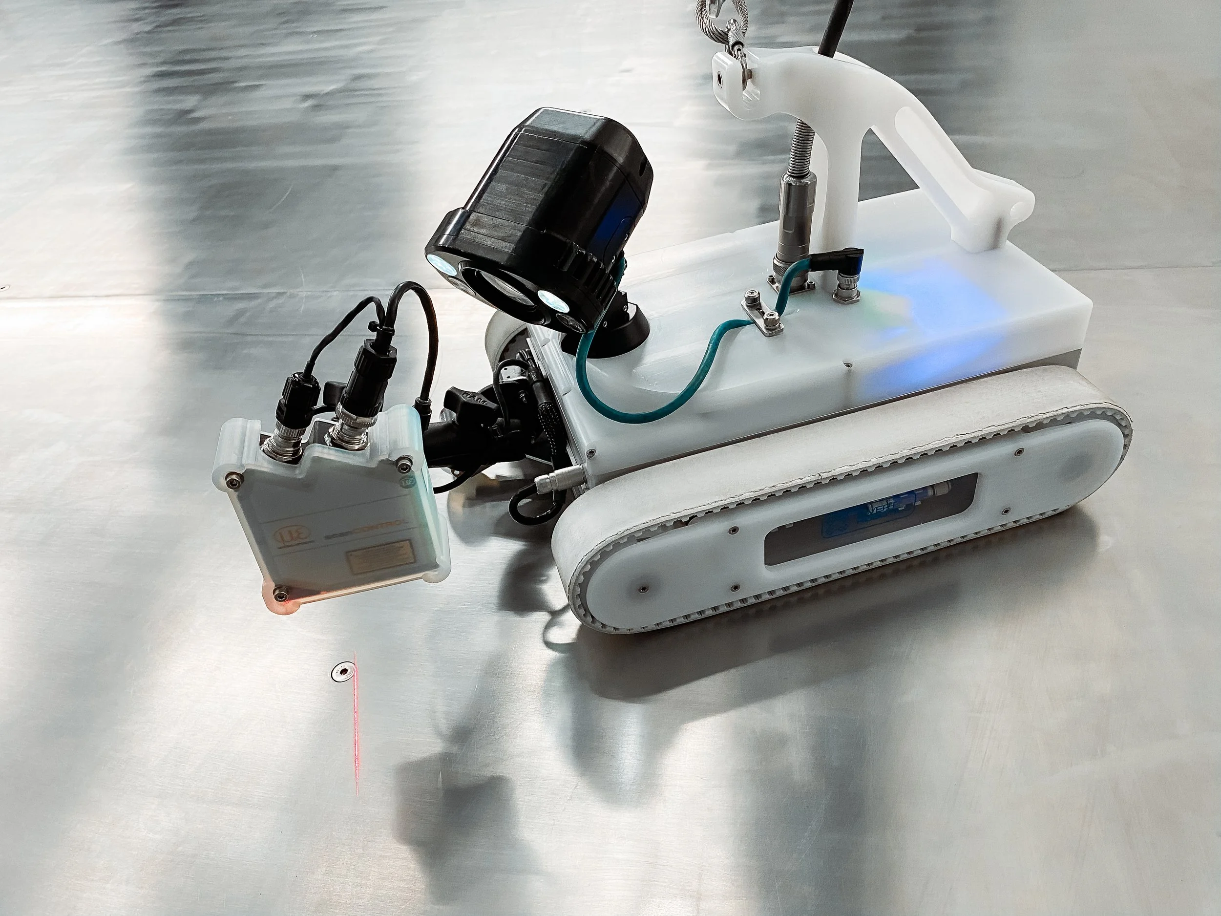 Close-up of an Invert Robotics robotic, with laser surface scanner tool and lights on a stainless steel surface.