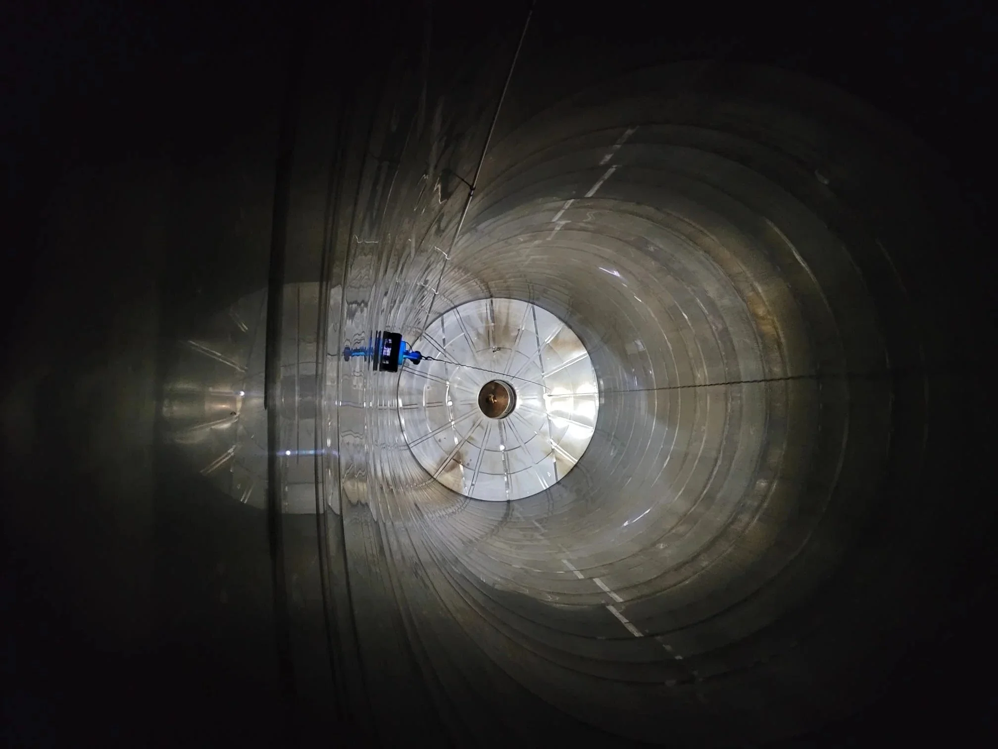Inside a large industrial tunnel or pipe with reflective walls and a robotr at the far end, possibly inspecting it.