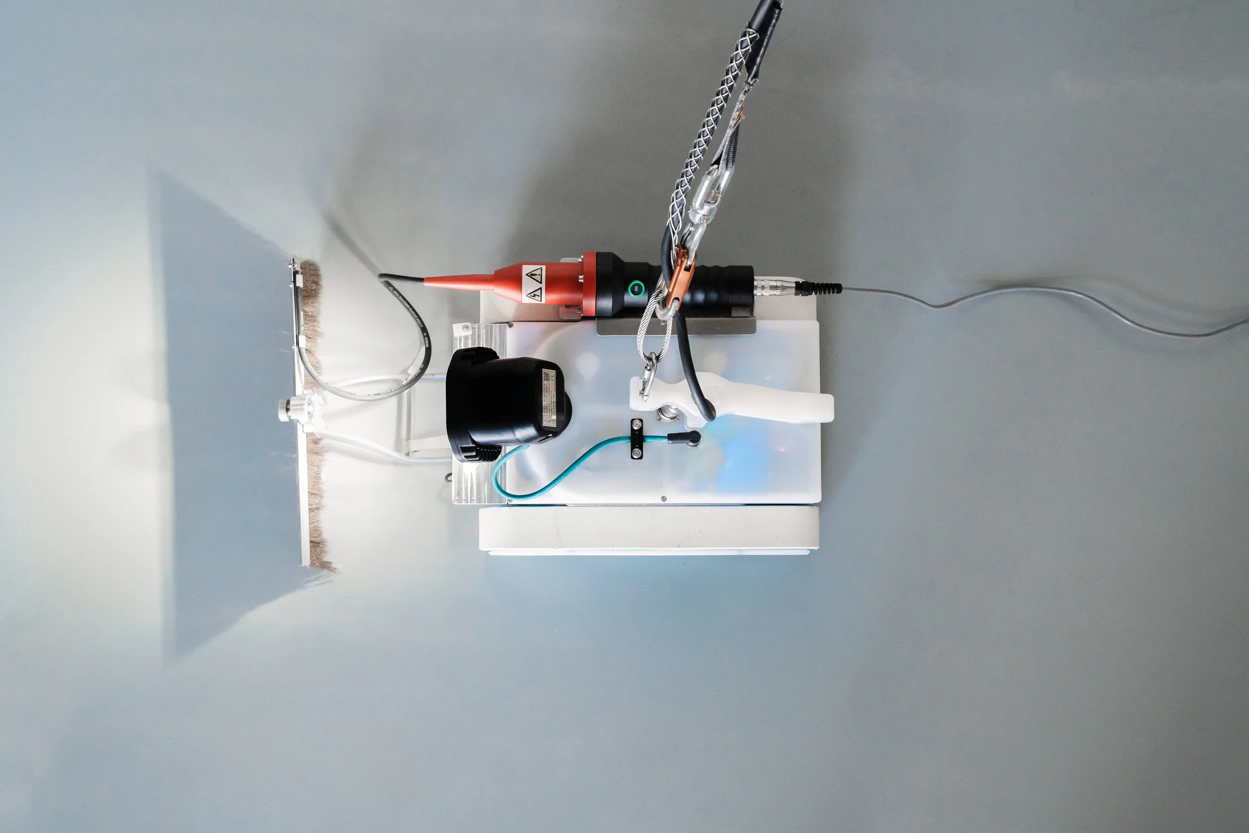 Close-up of an Invert Robotics robotic, with spark testing brush tool mounted to the front and lights on a stainless steel surface.