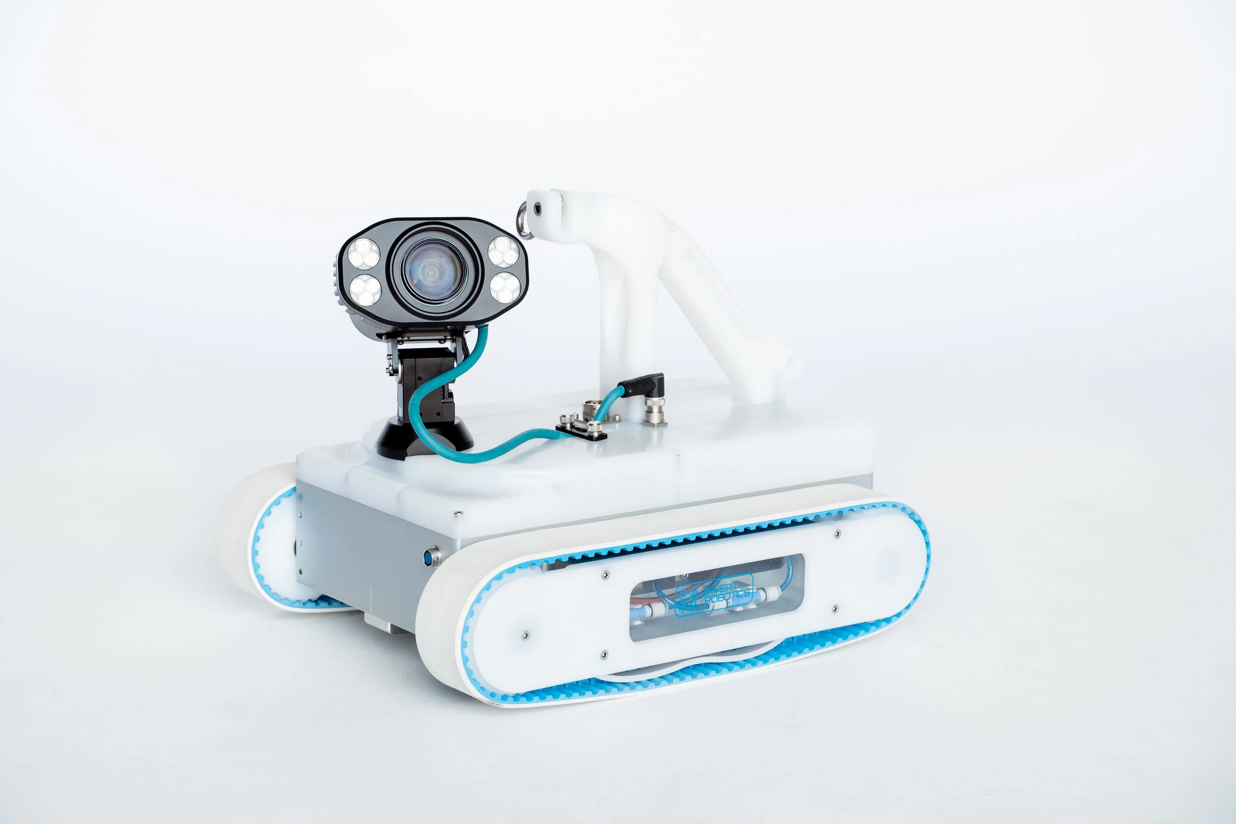 A Invert Robotics V1800 robotic device with tank-like treads, a camera, and multiple lights, set against a plain white background.