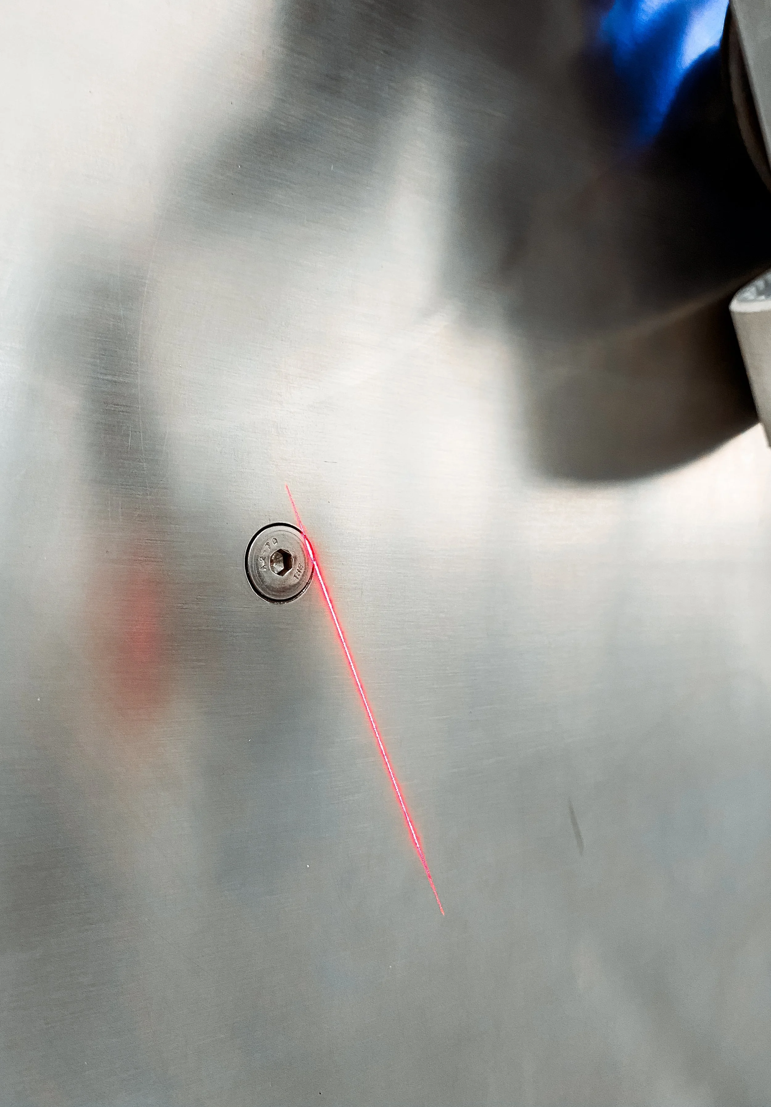 A red laser pointer beam on a stainless steel surface near a screw with a small hole.