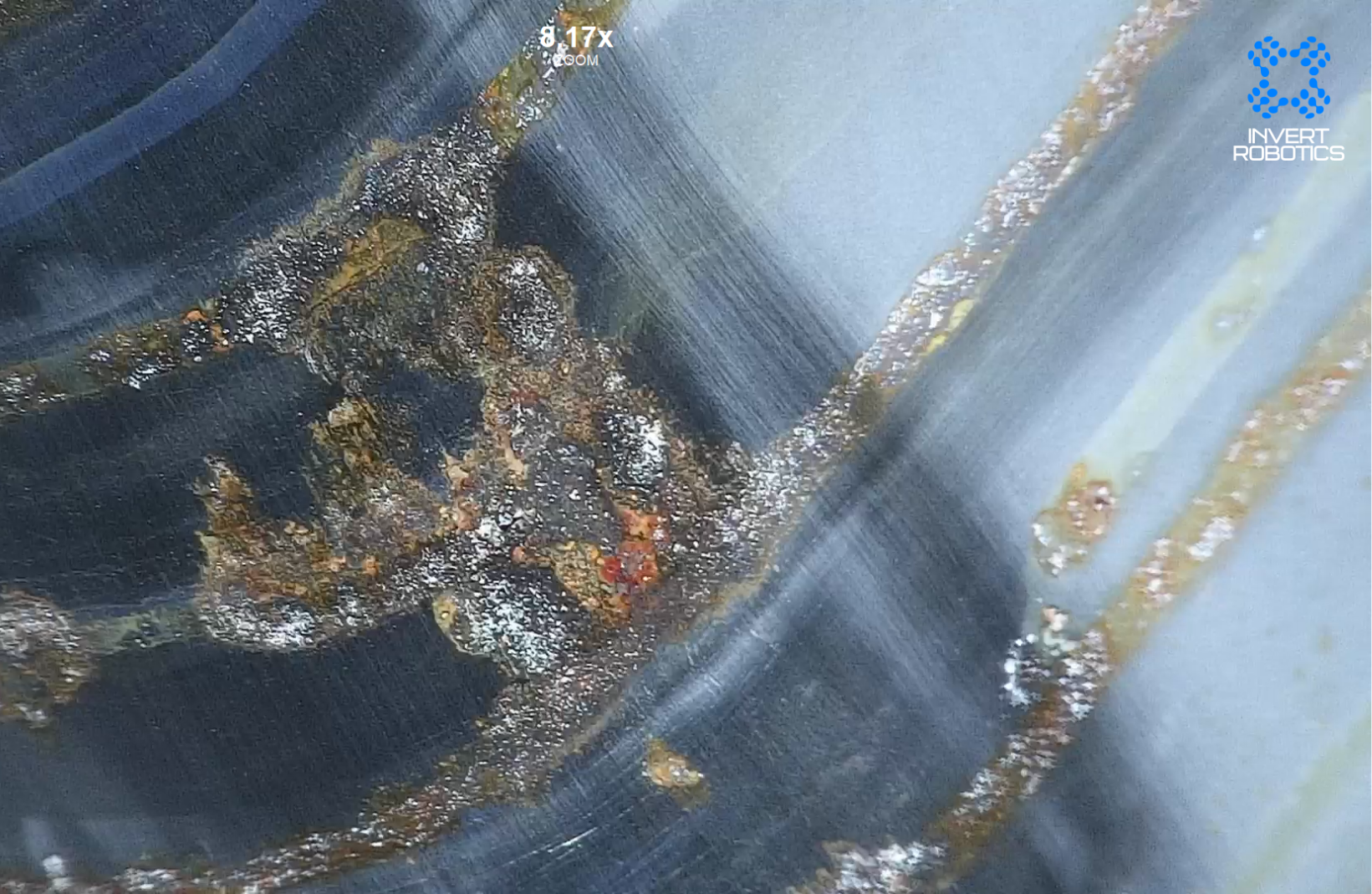 A robotic device submerged in water, with visible hoses and wires, with algae or debris on its surface, marked with the logo 'Invert Robotics'.