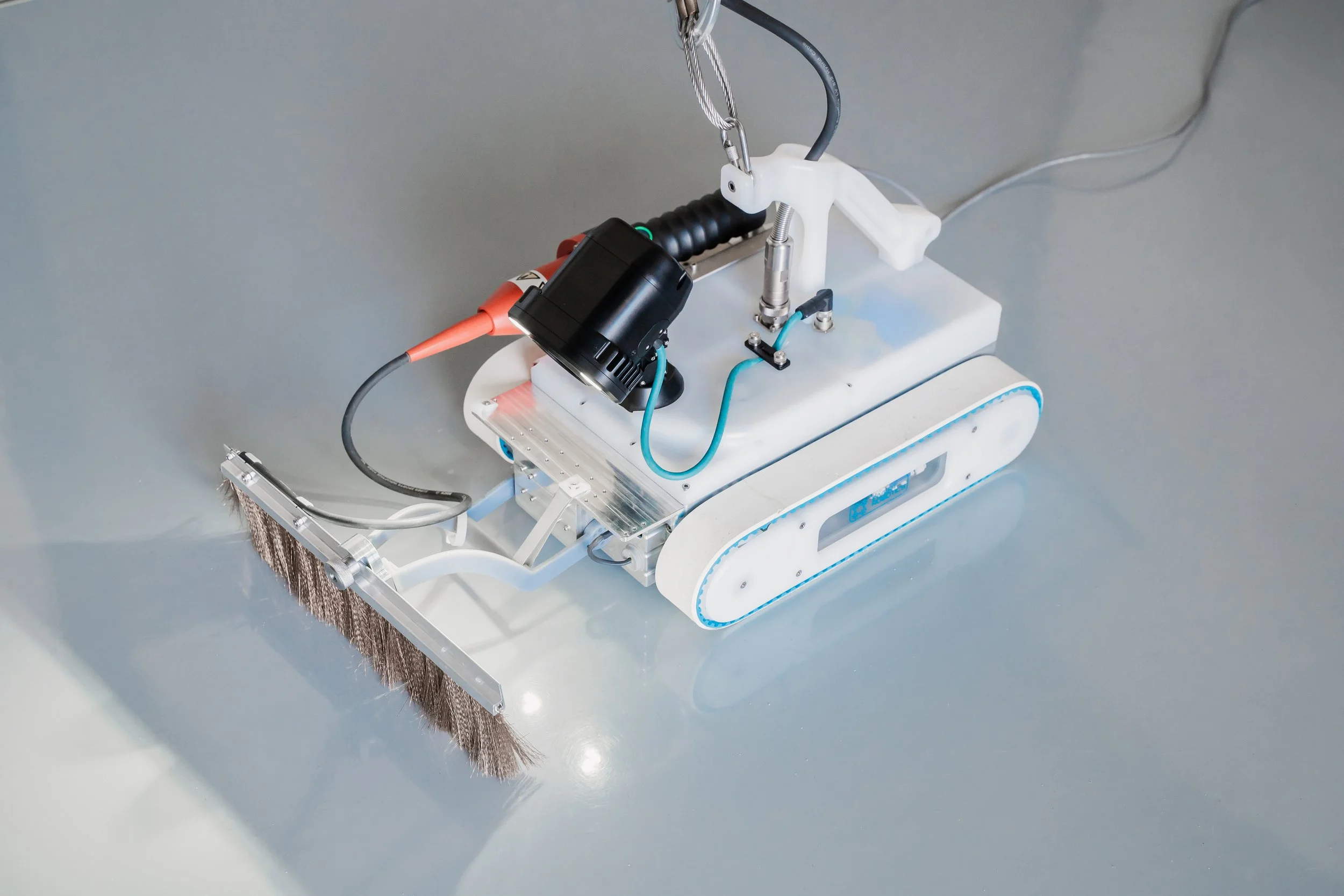 Close-up of an Invert Robotics robotic, with spark testing brush tool mounted to the front and lights on a stainless steel surface.