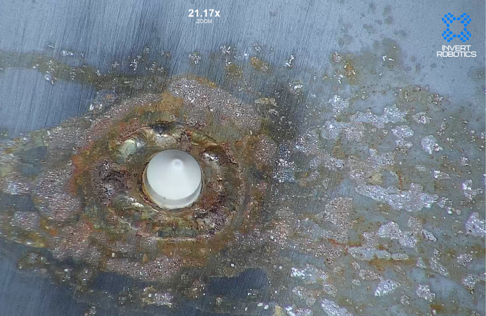 Close-up of a damaged surface with rust, corrosion, and an embedded white spherical object, with the logo 'INVERT ROBOTICS' in the top right corner.