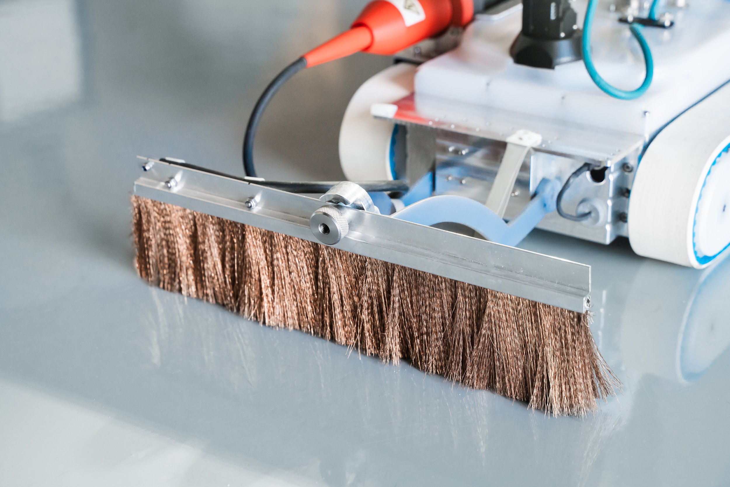 A close-up of spark testing tool with a copper-colored brush attached to a Invert robotics robot, connected to black and red cables, likely used inspection