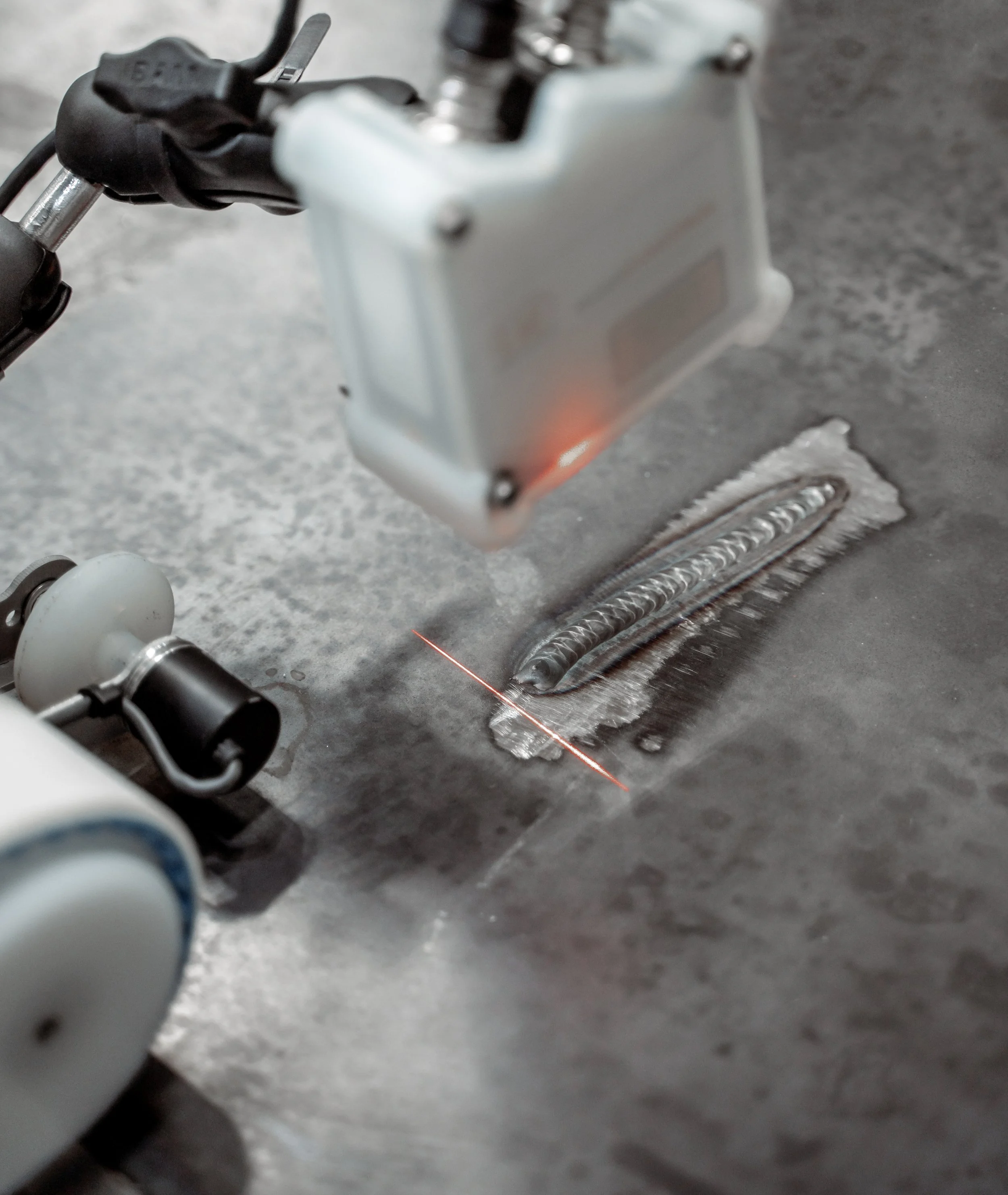 Close-up of a laser welding process on a metal surface with a laser pointer and welding equipment visible.