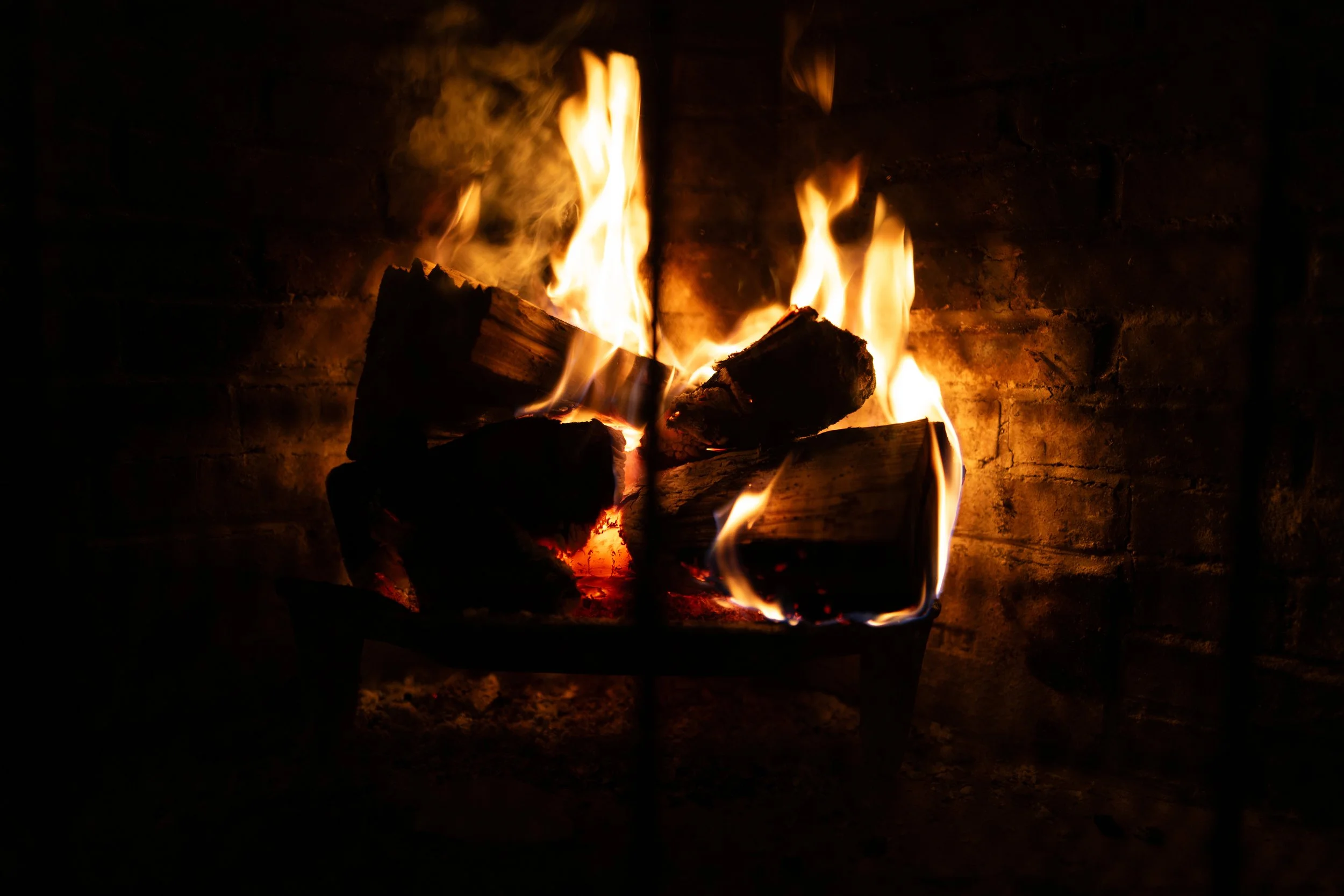 A fireplace with glowing logs and bright flames against a dark background.