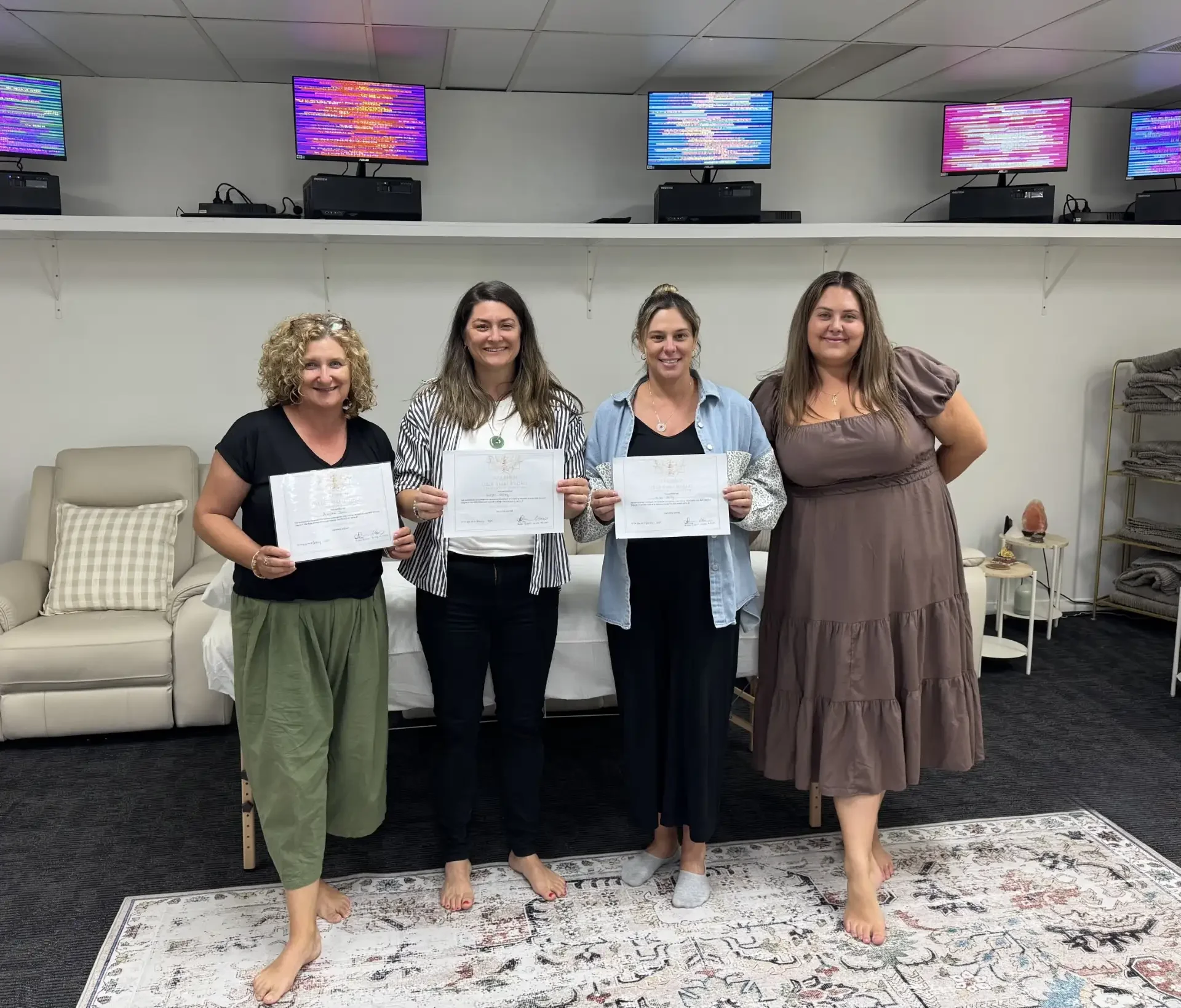 Four women standing and smiling while holding reiki completion certificates in front of a chakra banner