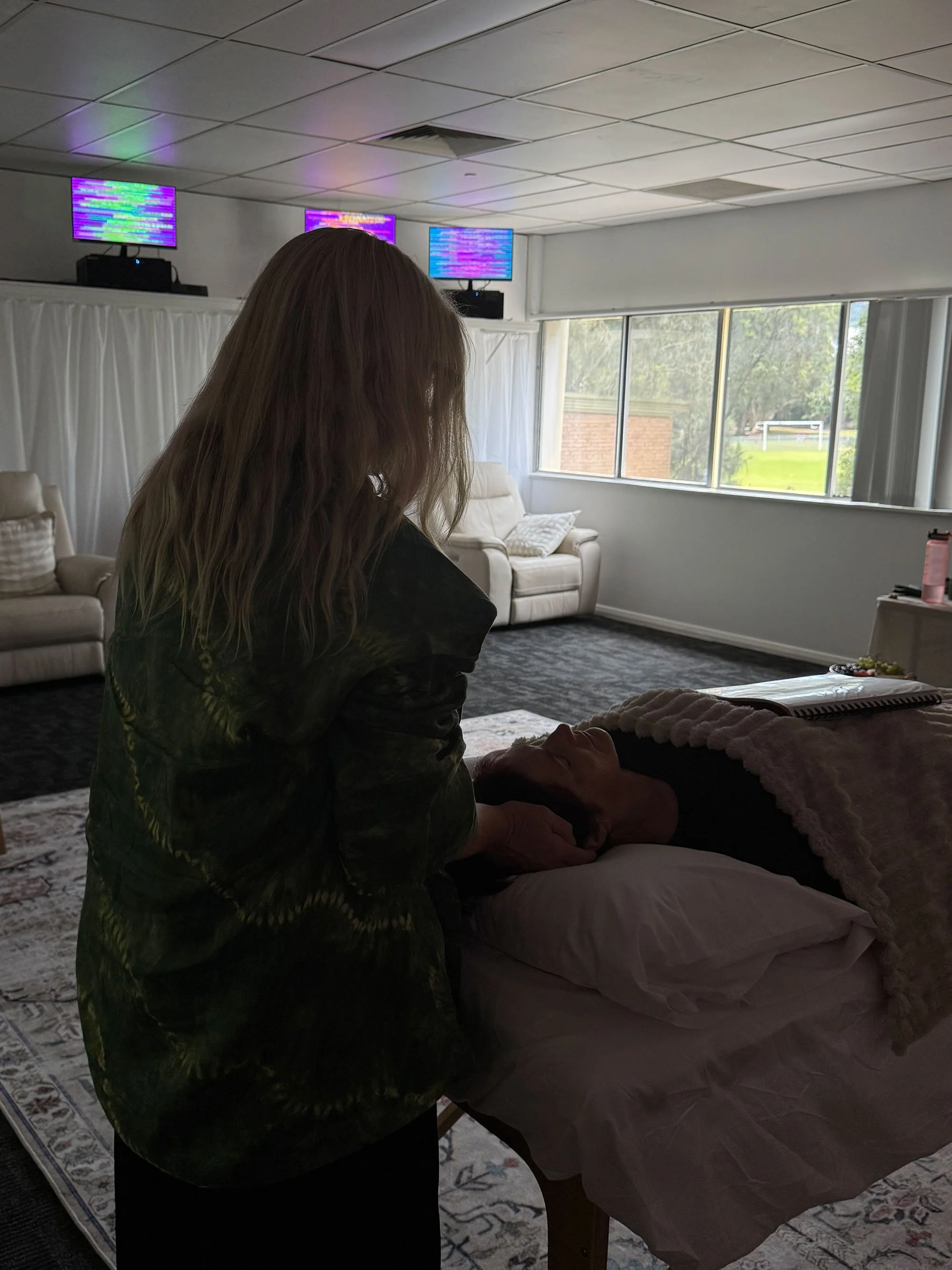 Woman in black performing hands-on reiki on a client at a treatment table in the Soulibrium Scalar Room