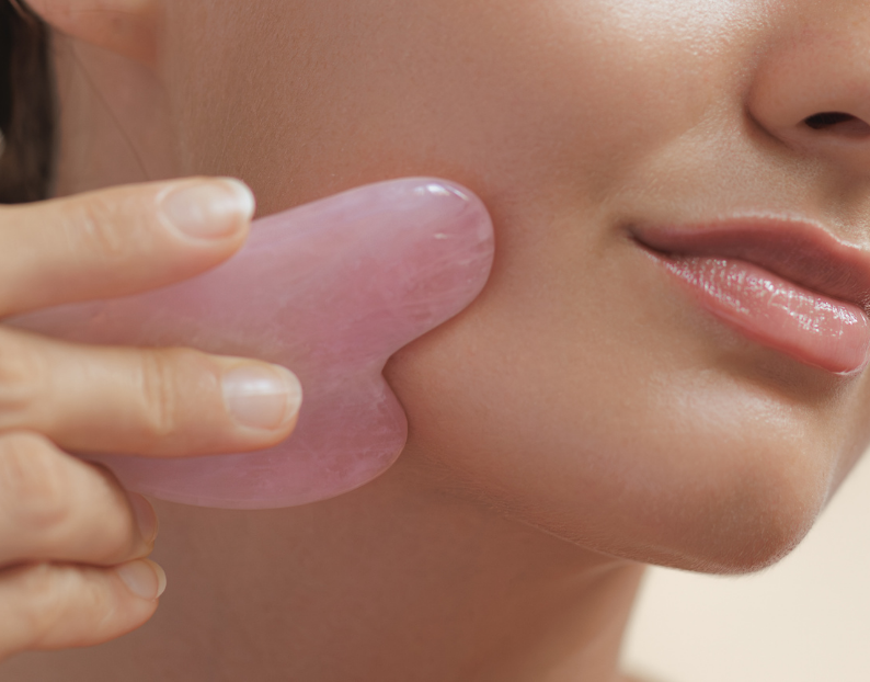 Woman holding a rose quartz crystal gua sha to her jawline