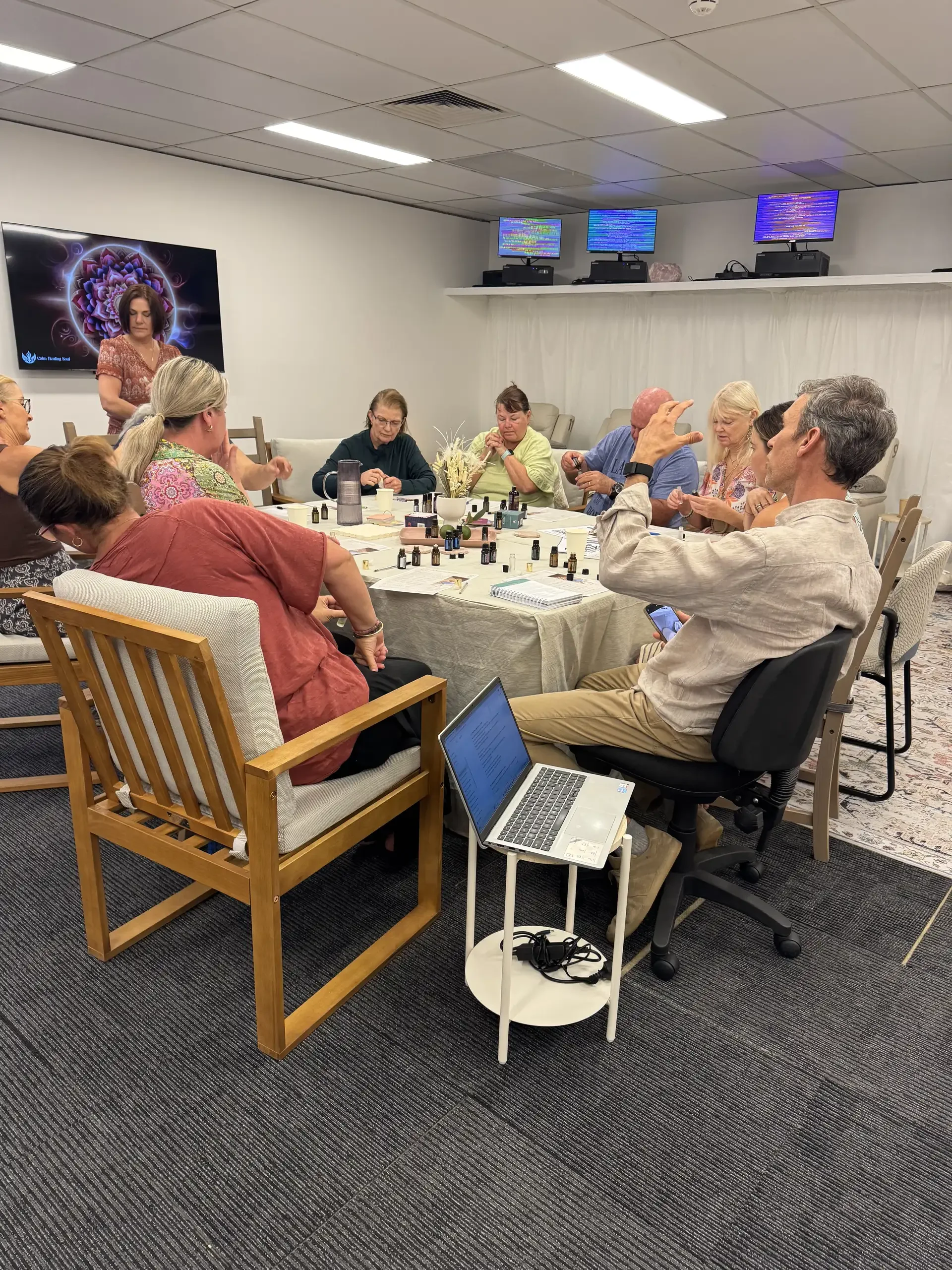 Community members seated around a table during a Soulibrium essential oils workshop with bottles and a laptop