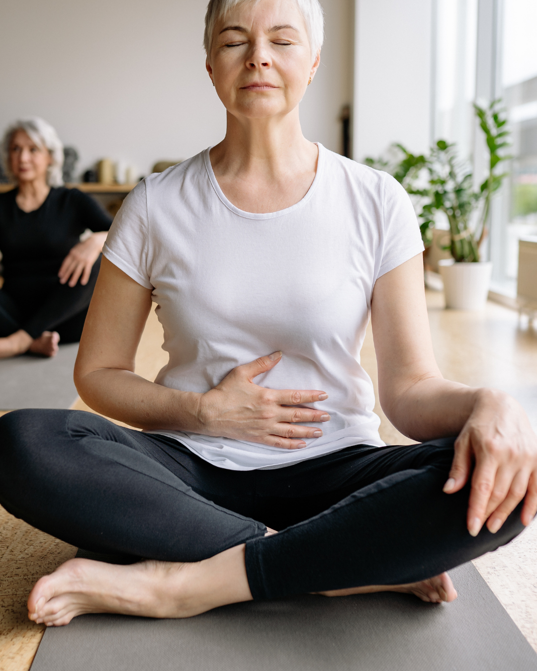 Woman seated cross-legged on a yoga mat with hands on chest and belly during a Soulibrium breathwork practice