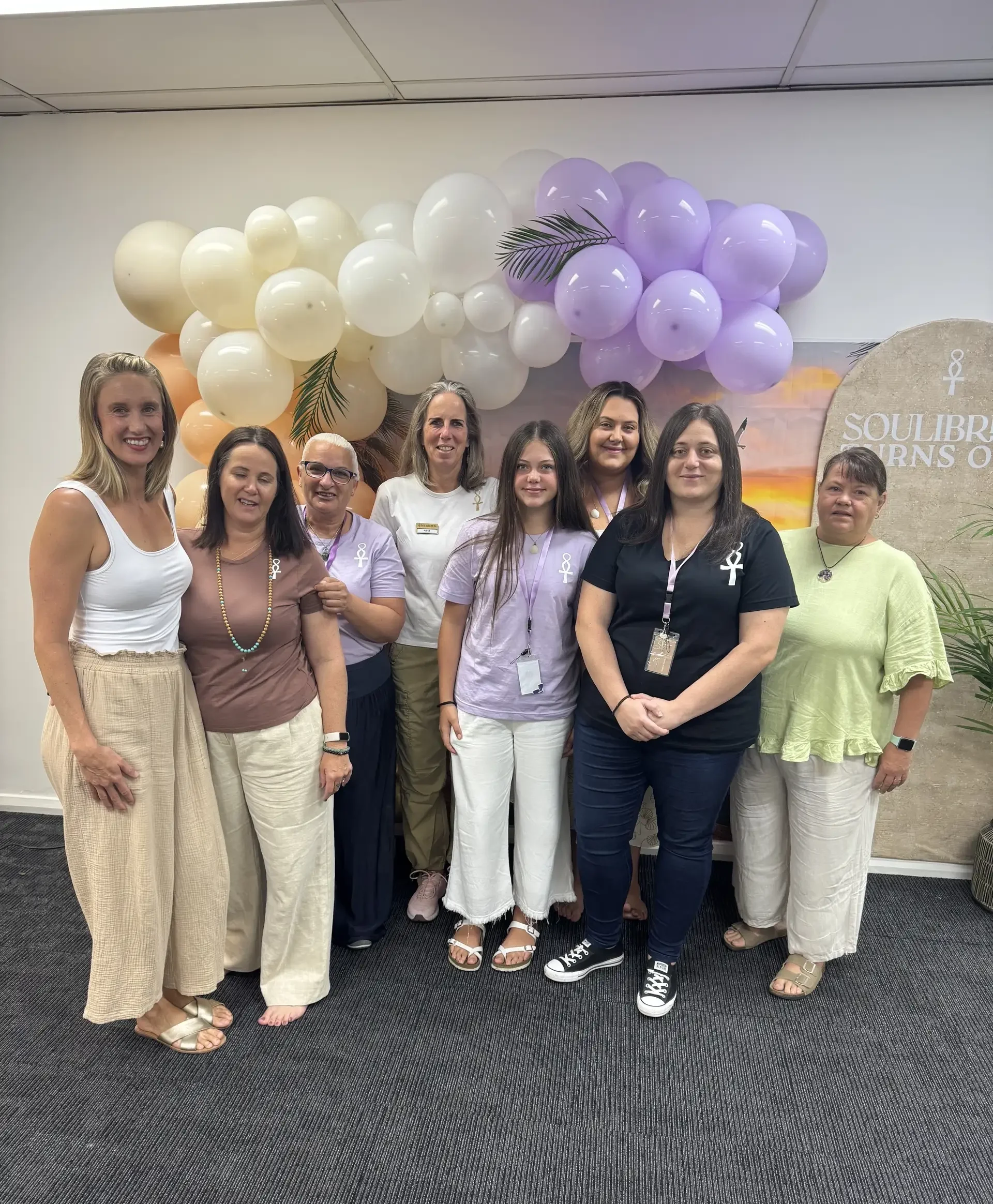 Group of eight women posing together at Soulibrium Turns One anniversary celebration with balloon arch