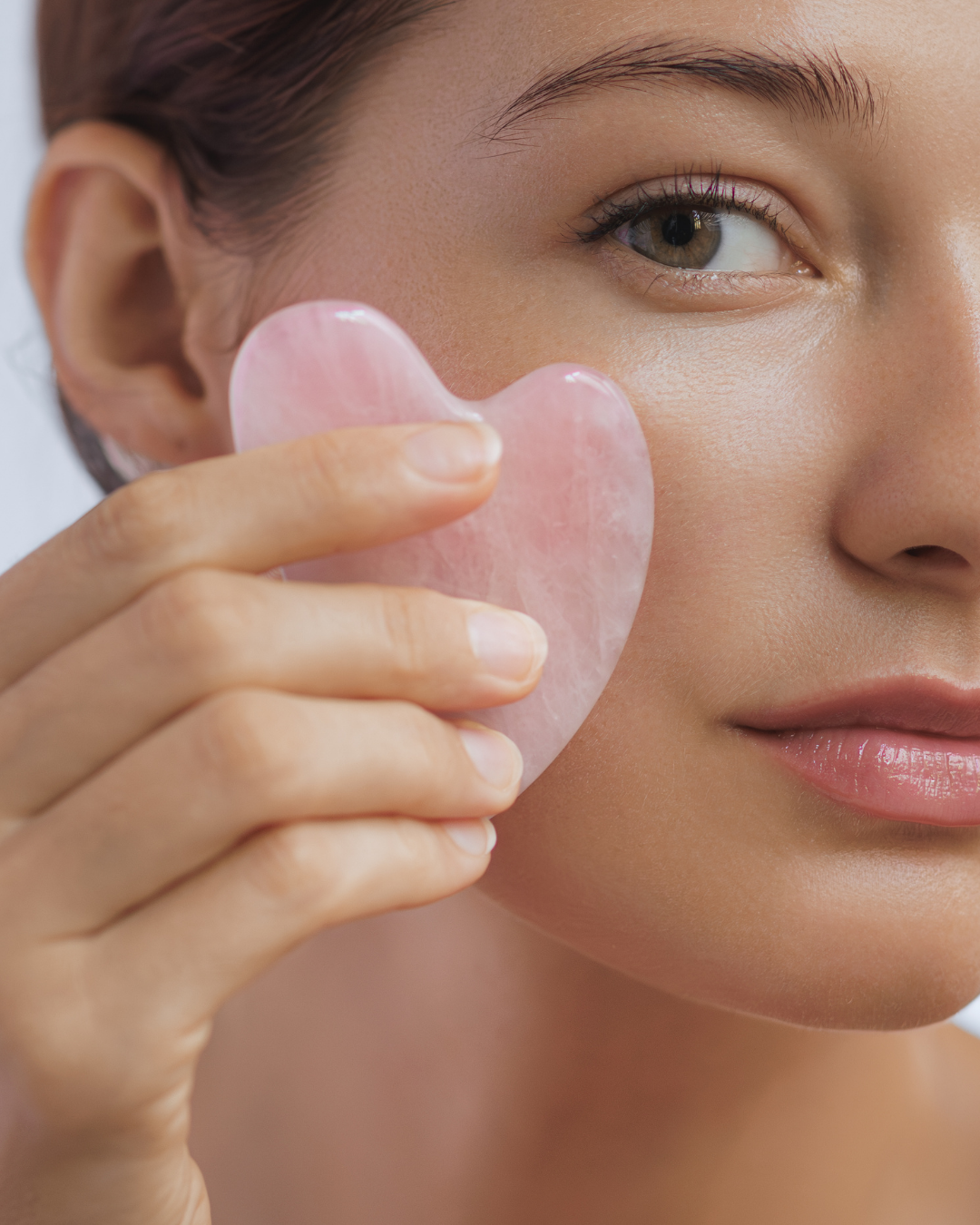 Woman holding a rose quartz crystal gua sha tool to her face
