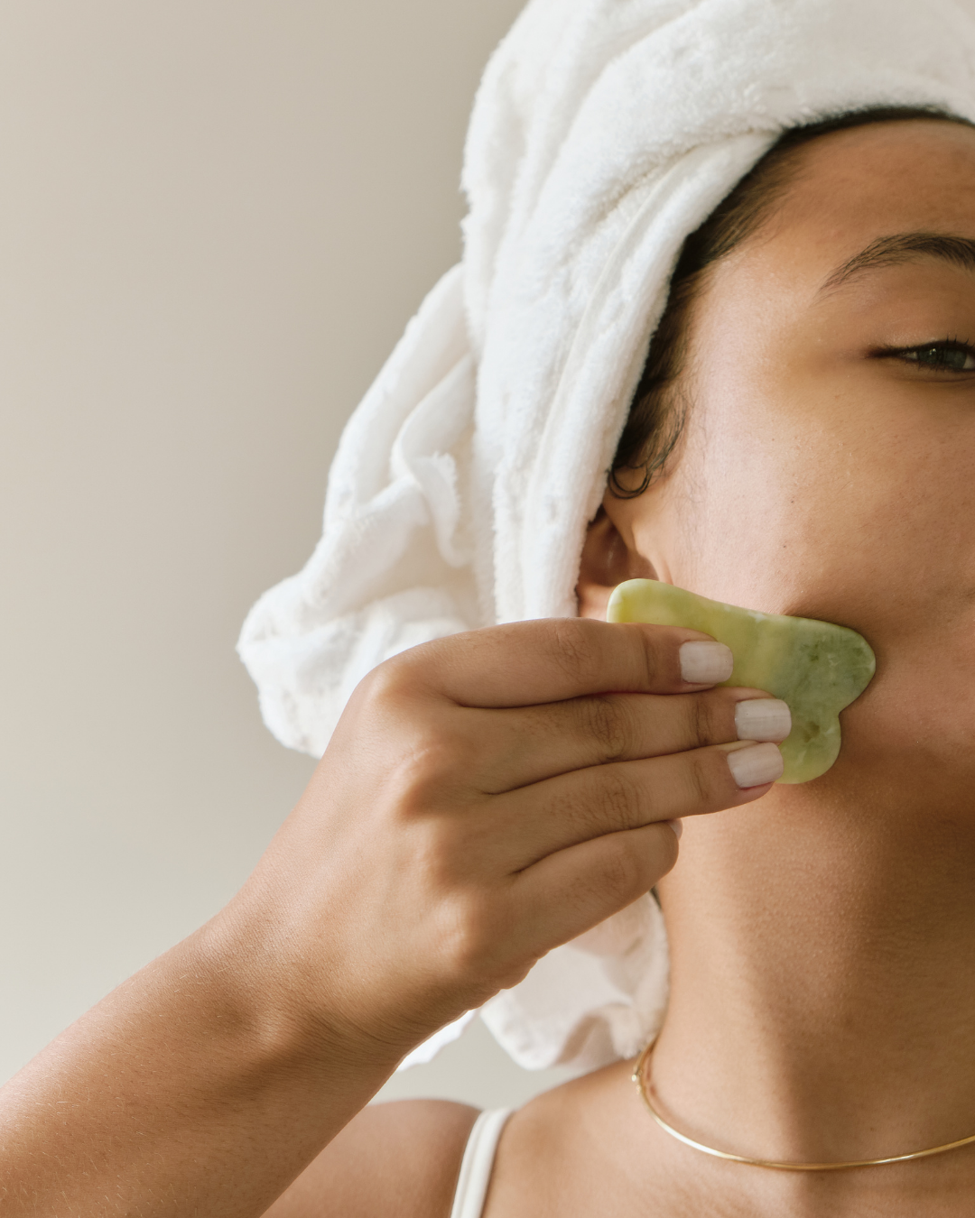 Women using a jade gua sha crystal along her jawline