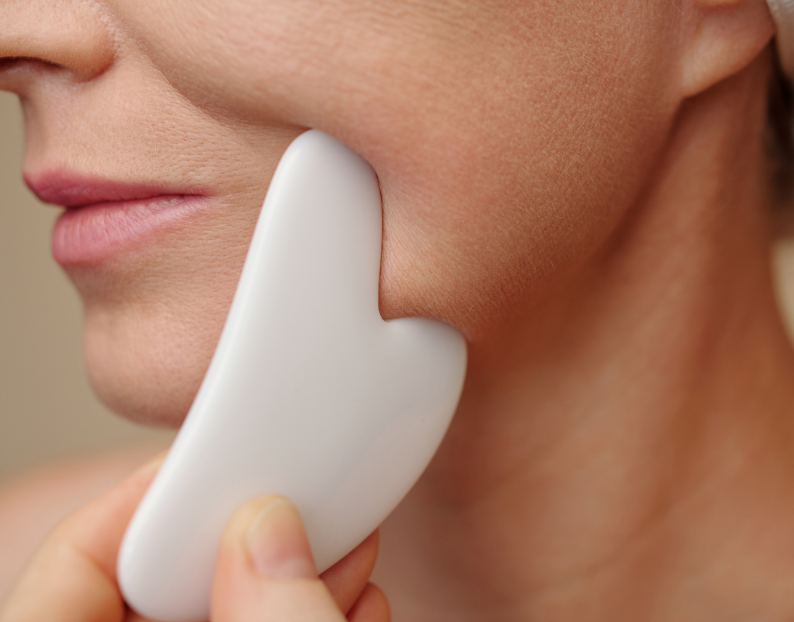 Woman massaging her jawline with a quartz crystal gua sha tool