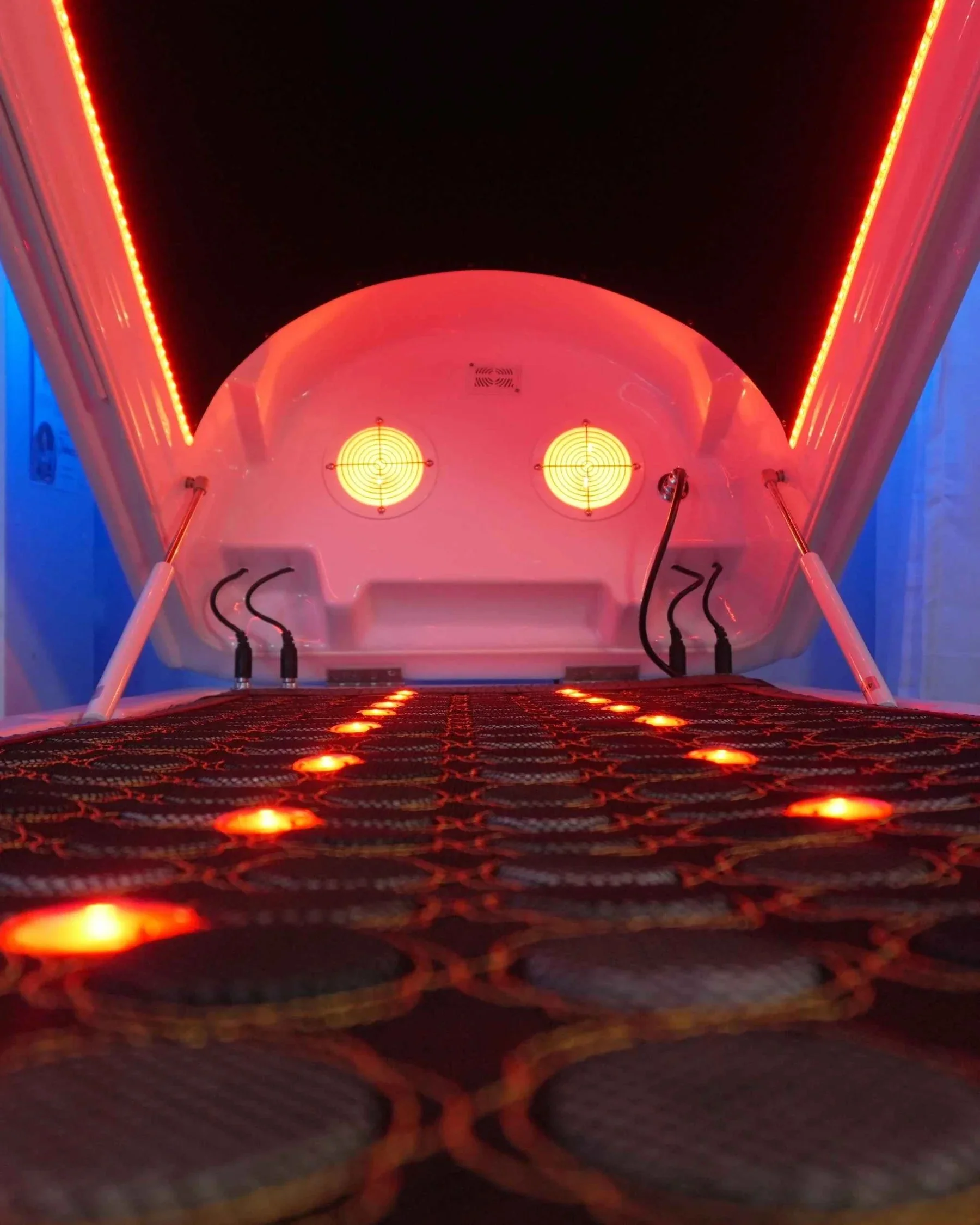 Close-up interior view of Soulibrium Wollongong infrared sauna pod showing red heating lights along the bed surface and circular infrared emitters