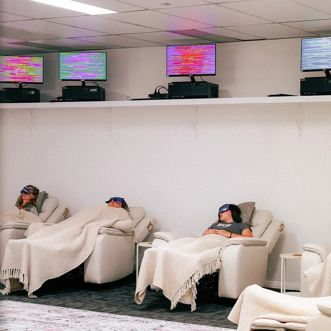 People laying in recliner chairs in the Scalar Room at Soulibrium Wellness Centre in Wollongong where the EE-System plays on monitors on the wall.