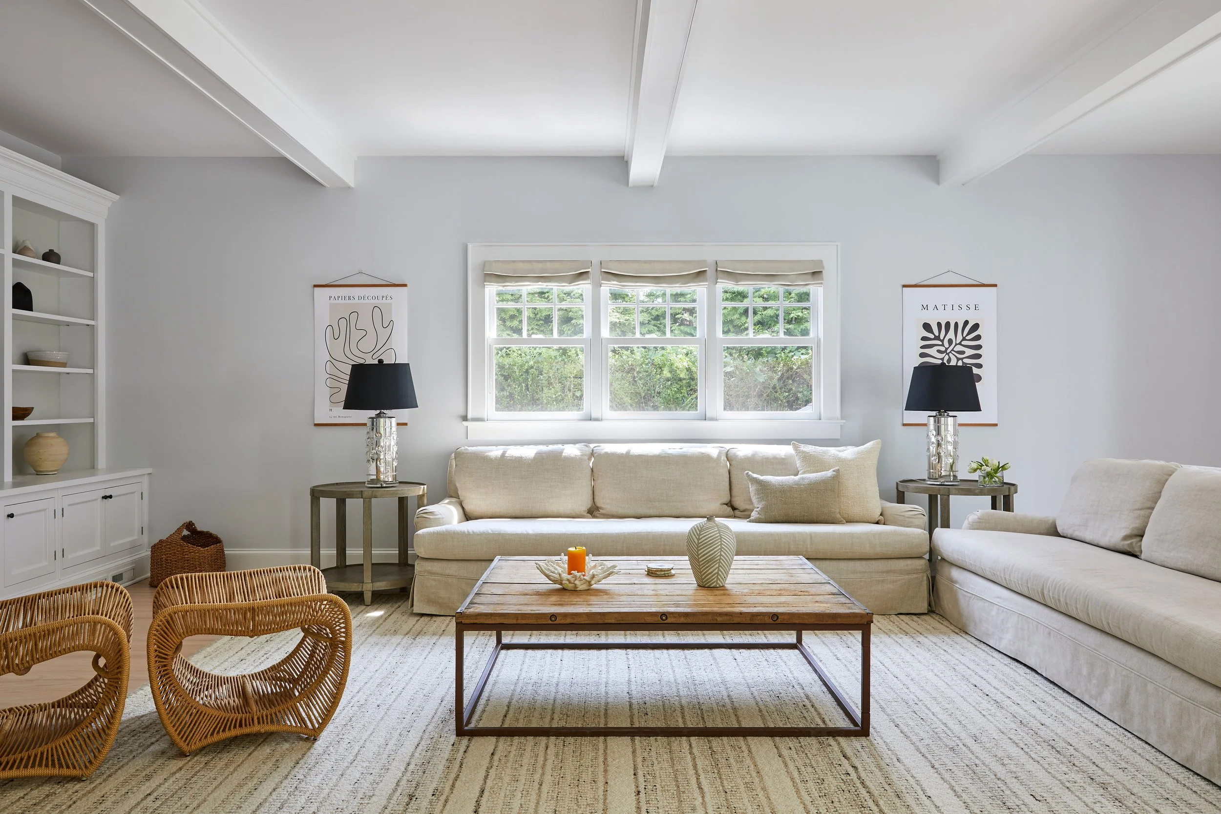 Coastal family room with sand linen sofas, rope lounge chairs, raw wood and iron coffee table, and Matisse posters in a Southampton NY home by Ginger Lemon Indigo