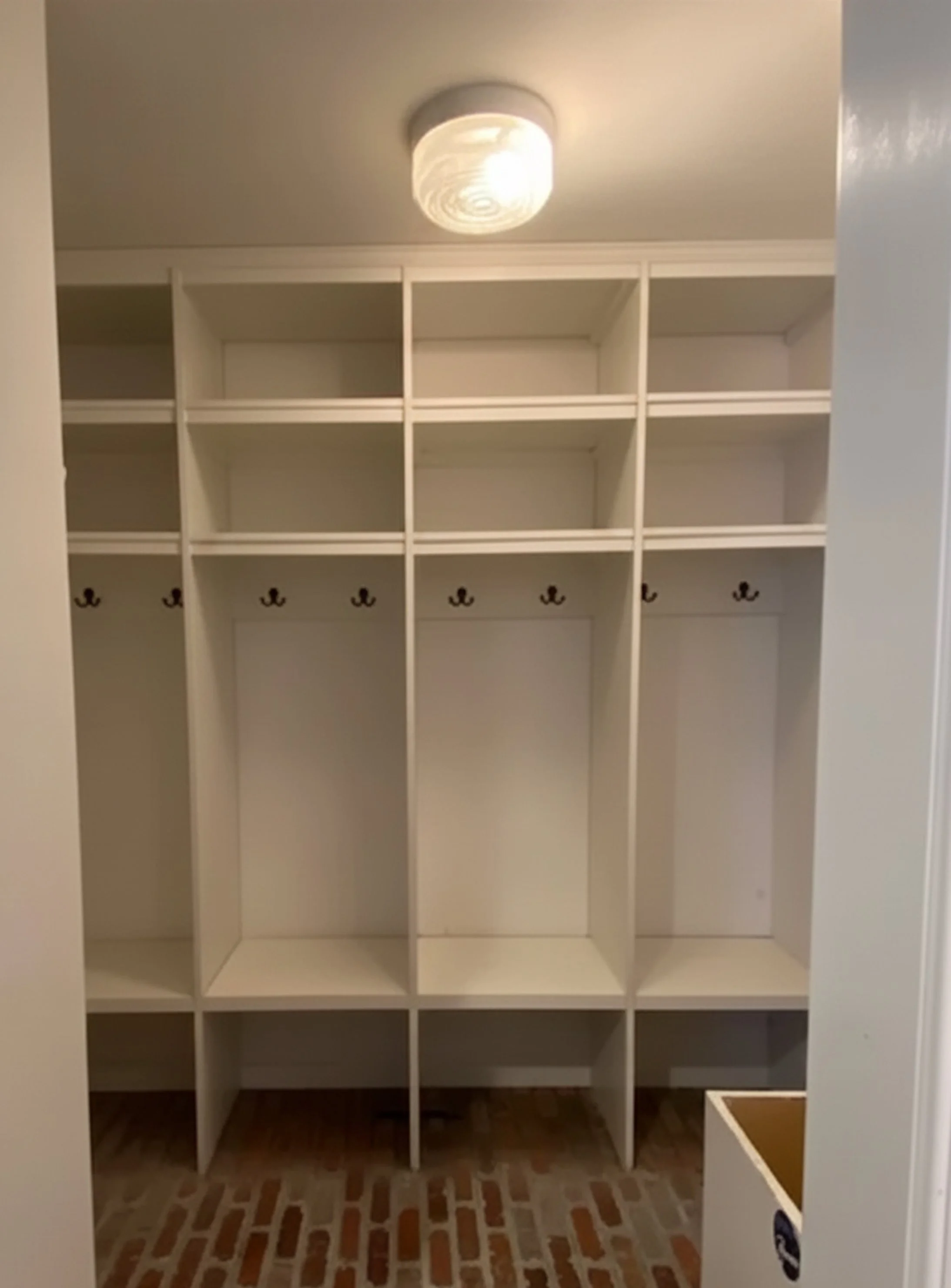 Darien mudroom before renovation, white open cubbies, single ceiling fixture and no storage below the bench