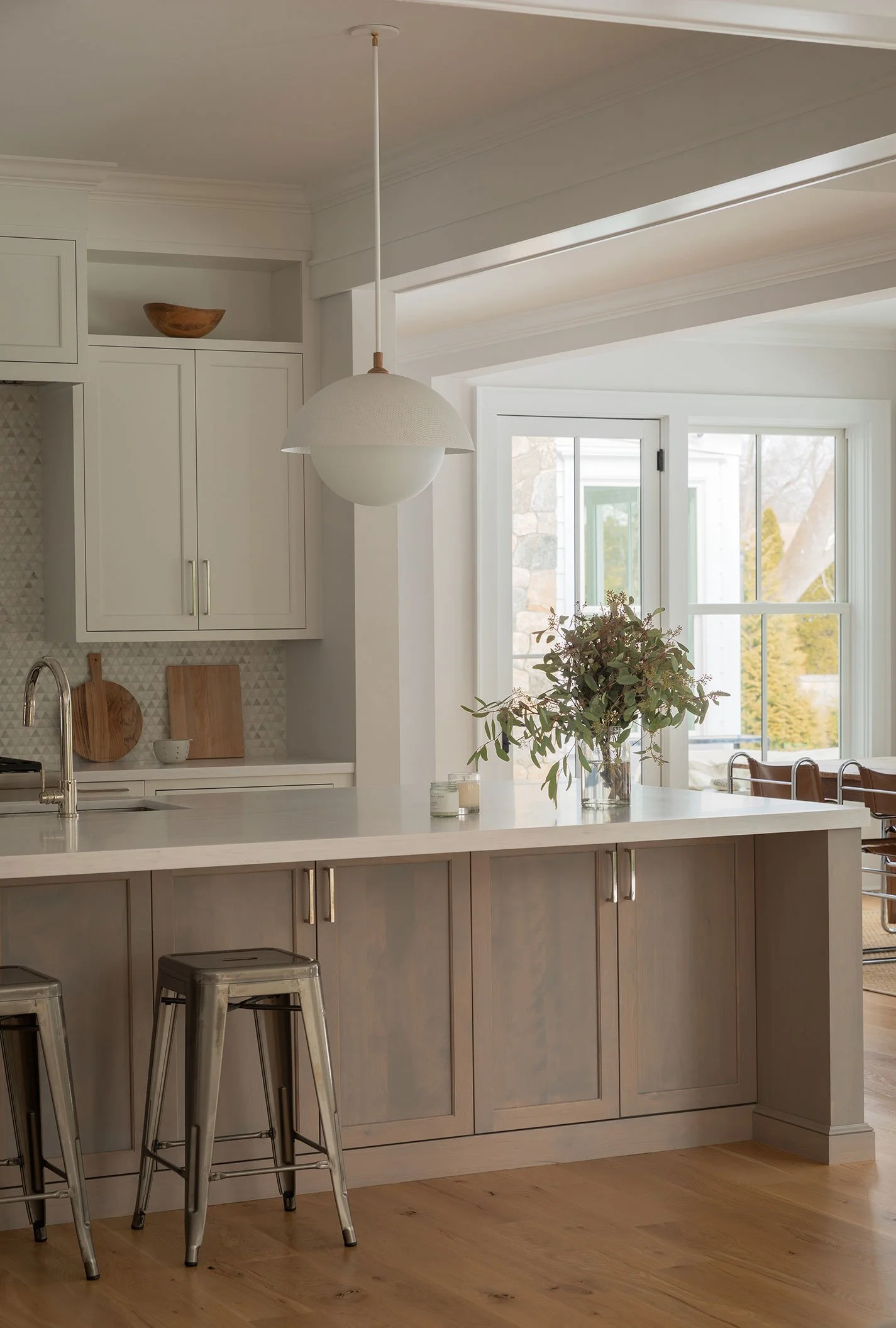 Westport CT kitchen with greige island, quartz counter, triangular marble mosaic backsplash, globe pendant and chrome counter stools