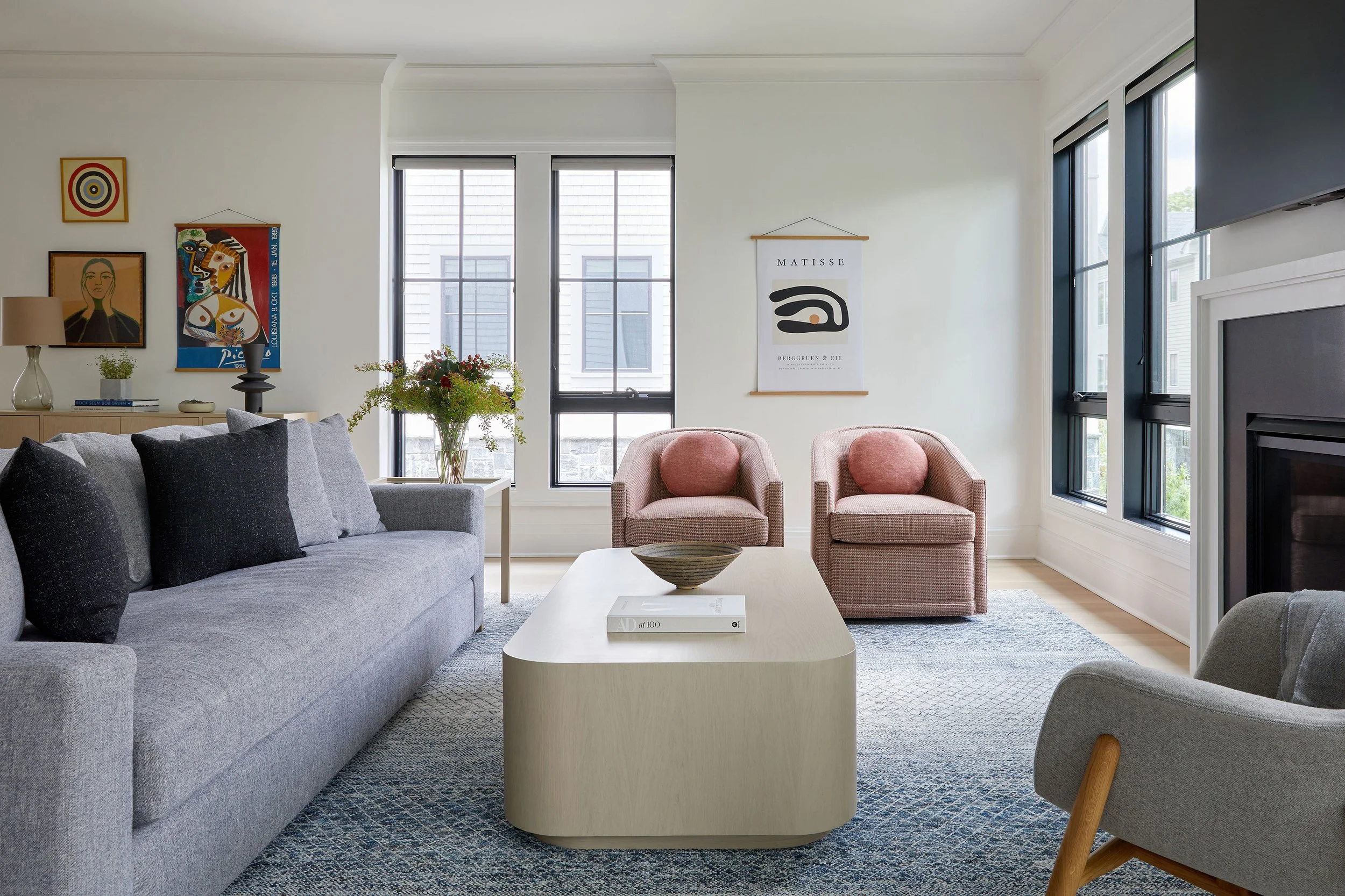 Open plan living room with grey sectional, rounded coffee table, pink swivel chairs, Matisse poster, and curated art wall in a Rye NY modern condo by Ginger Lemon Indigo