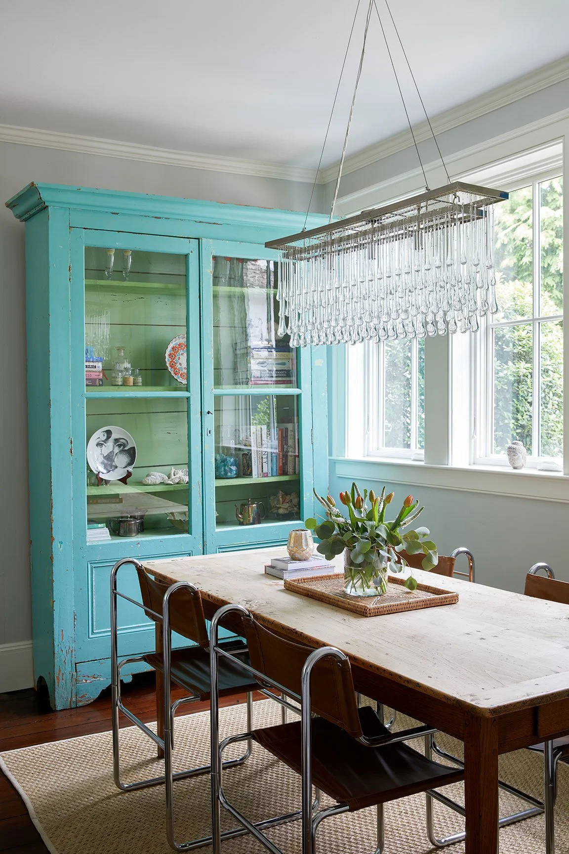 Kitchen with antique turquoise painted cabinet, raw wood farm table, chrome dining chairs, and crystal drop chandelier in a Darien CT eclectic farmhouse by Ginger Lemon Indigo