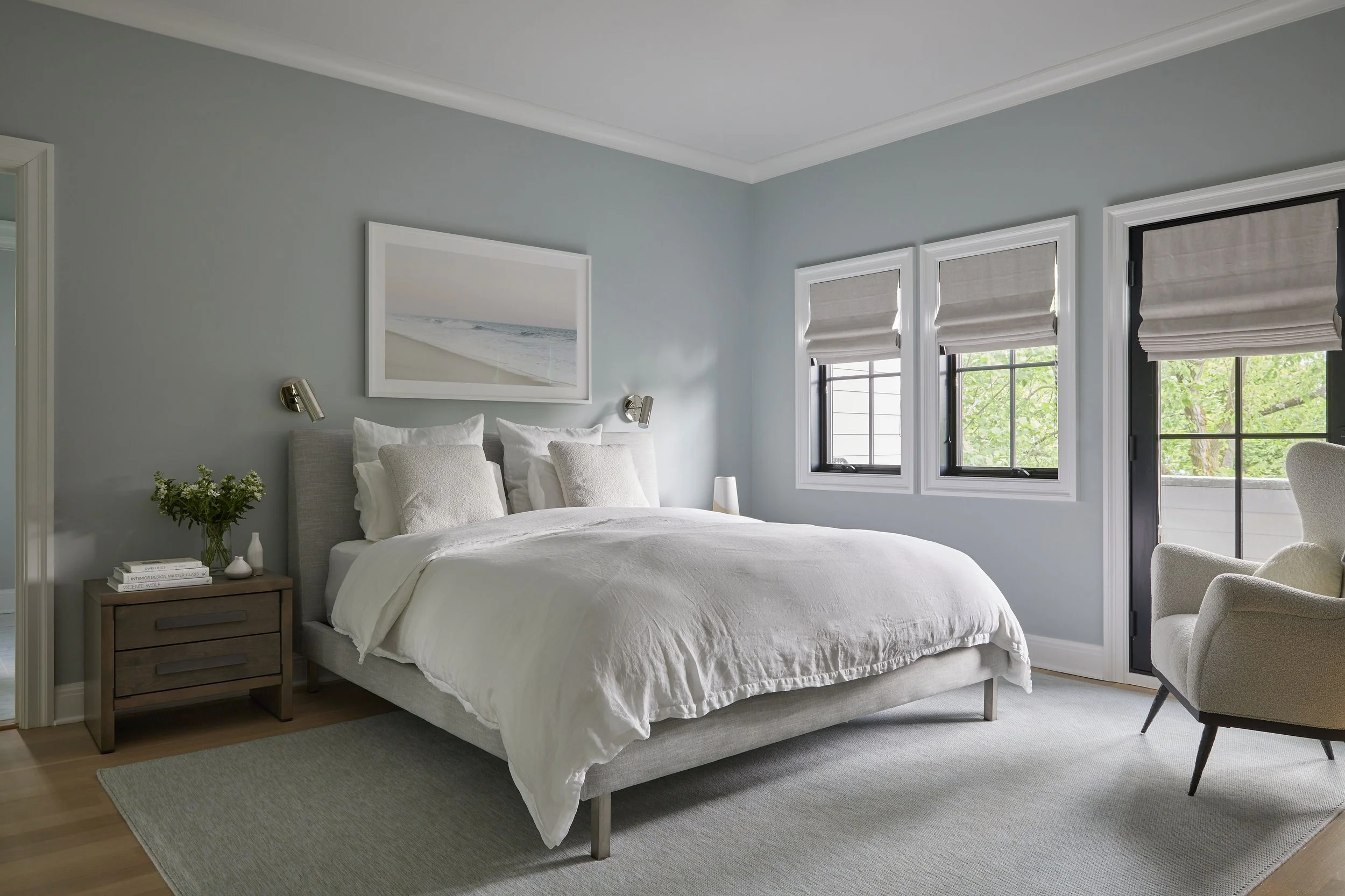 Primary bedroom with seafoam walls, upholstered headboard, Cas Friese beach photograph, wall sconces, and linen roman shades in a Rye NY condo by Ginger Lemon Indigo